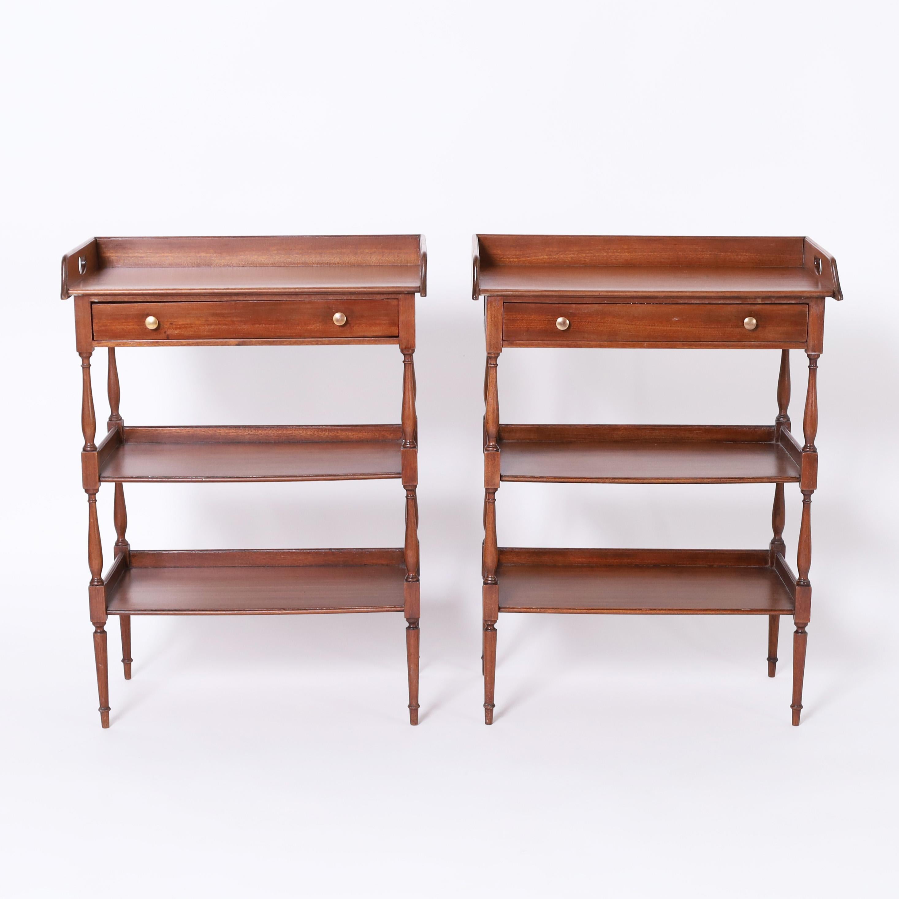 Handsome pair of English stands crafted in mahogany with an attached tray form top over two lower tiers having elegant turned supports on tapered legs.