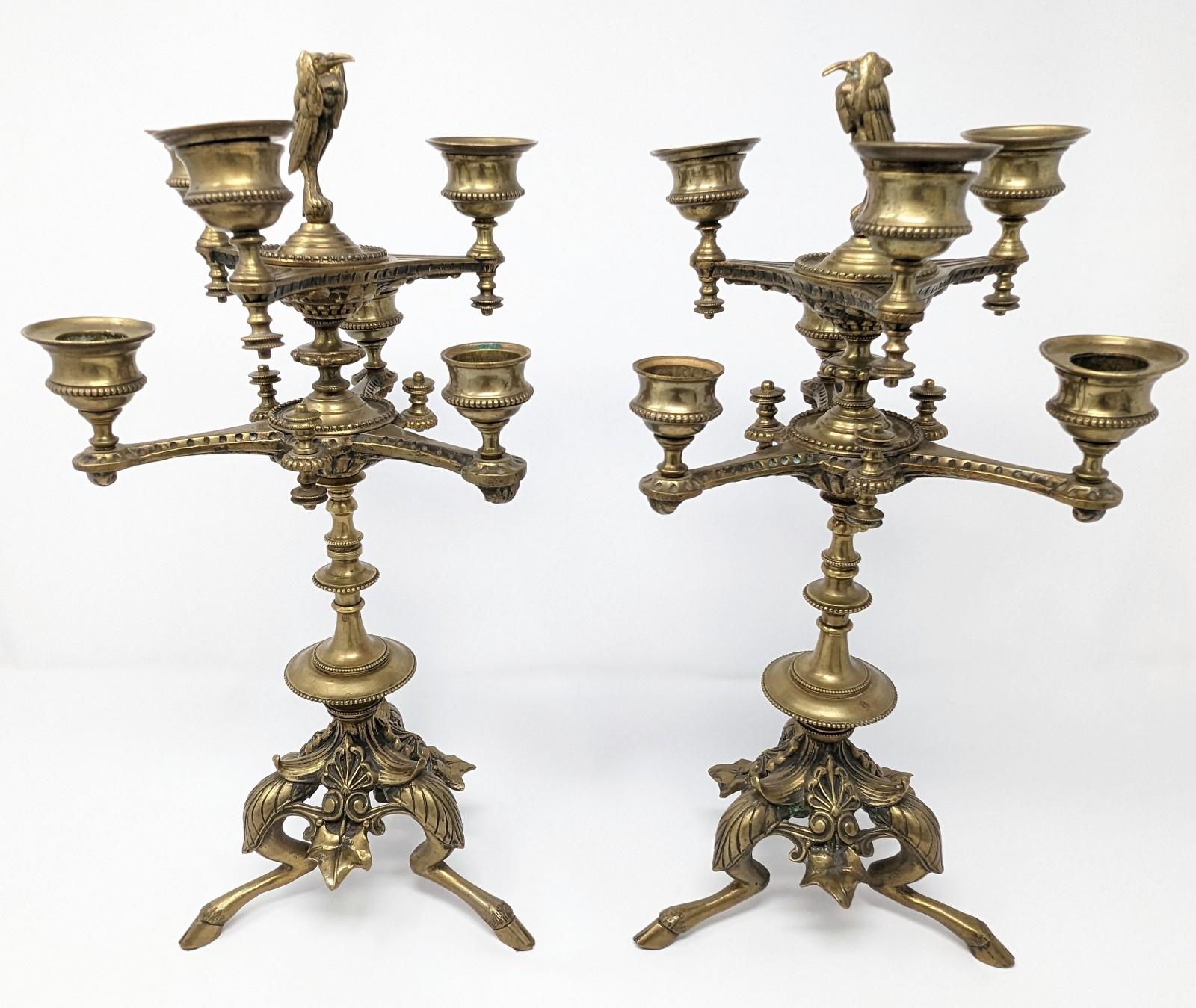 Pair of exquisite antique patinated brass candelabras with ornate fawn hoof feet and elegant bird tops. Measures 7.25 inches at its widest points by 15 inches in height. There is a hint of a makers mark on one of them as photographed, however we are