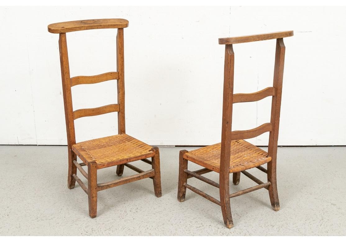 Une belle paire de chaises de dressage primitives de style campagnard français. Des cadres en bois dur adouci par le temps avec des rails de crête plats et courbés sur les dossiers à lattes hautes et profilées. Les sièges cannelés à la main reposent