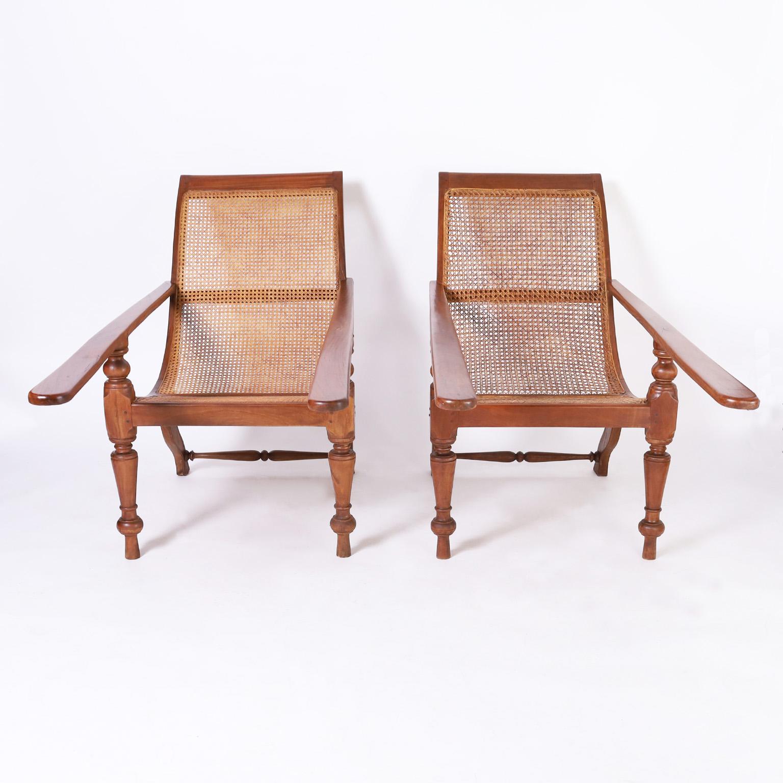 Intriguing pair of early 20th century British Colonial plantation chairs handcrafted in indigenous mahogany with elegant form featuring caned backs and seats, pegged construction, boot planks and Classic turned front legs. 

.