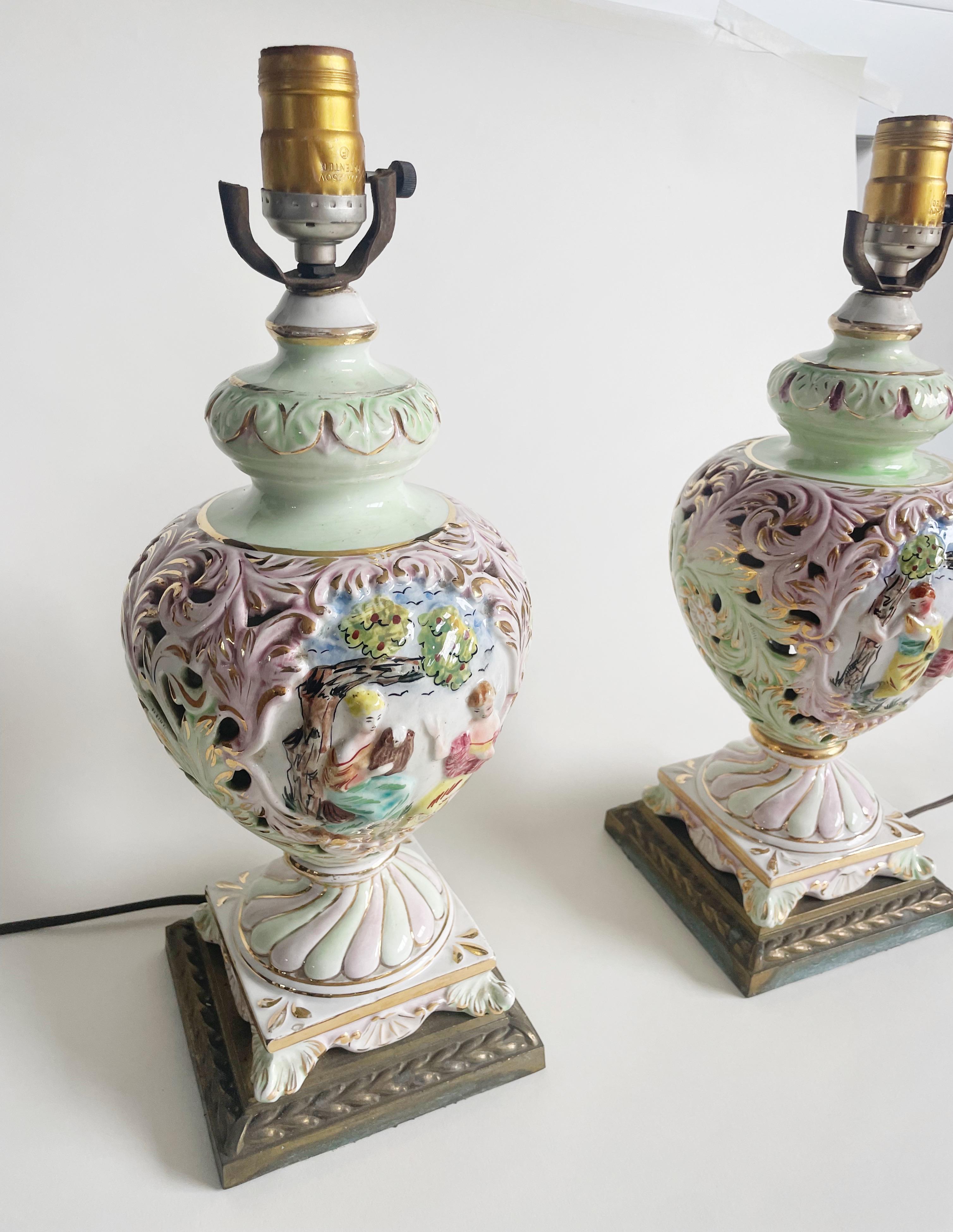 Add a touch of elegance to your living space with this beautiful pair of antique Capodimonte table lamps. Made in Italy, these lamps feature high relief porcelain and brass accents, giving them a unique and exquisite look. The lamps are corded