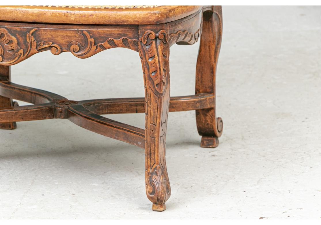 Fauteuils im Stil Louis XV, Typ Grand Mere, mit niedrigen Sitzen. Schön geschnitzte Nussbaumrahmen mit verdunkelten Blättern und verschnörkelten Rankendetails auf den Rückseiten der Stöcke. Mit geschwungenen Armlehnen und breiten Rohrsitzen mit