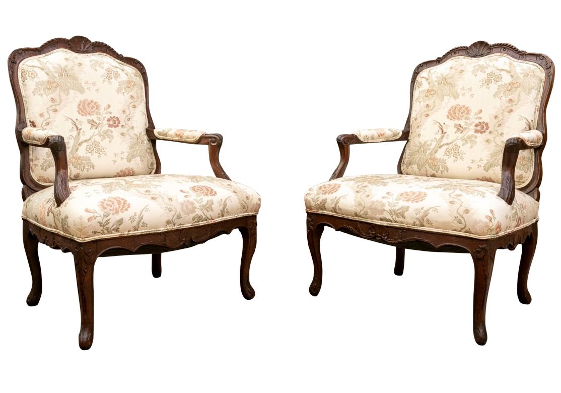 Pair of vintage carved oak Louis XV style fauteuil with serpentine front, carved apron, beaded carvings and surmounted with carved shell motif. The chairs with manchettes, the upholstery double welted in a cottony damask fabric with embroidered