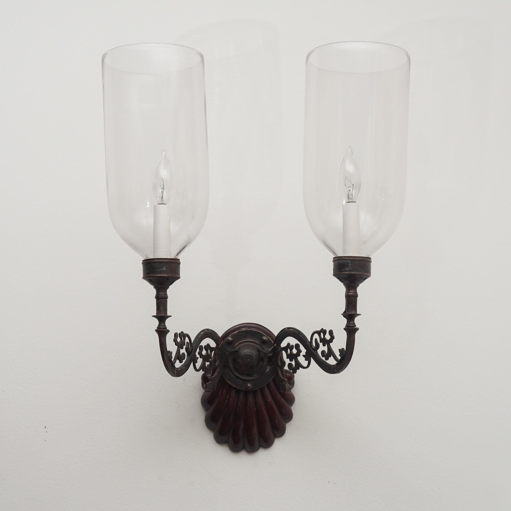 The antique carved rosewood wall sconce (one of two), shown here, is the perfect reflection of 19th century elegance. Featuring a shell carved rosewood wall mount, the sconce is enhanced with ornate metal work supporting two candle lights with clear