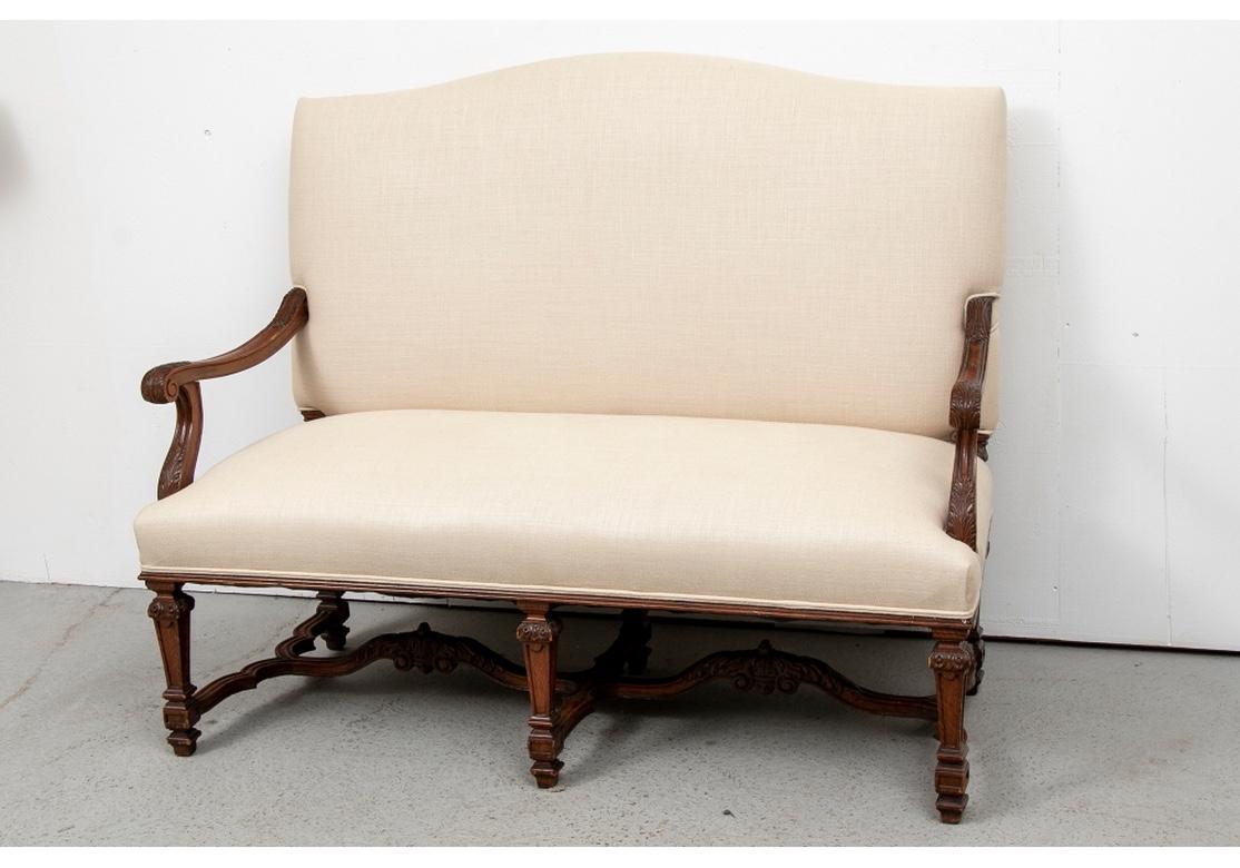 Ca. 1910. With a camel back and carved arms with acanthus leaves. Raised on a finely carved base with square tapering legs and carved serpentine stretchers. The long middle stretcher with carved acanthus scrolls on both ends. Custom upholstery in an