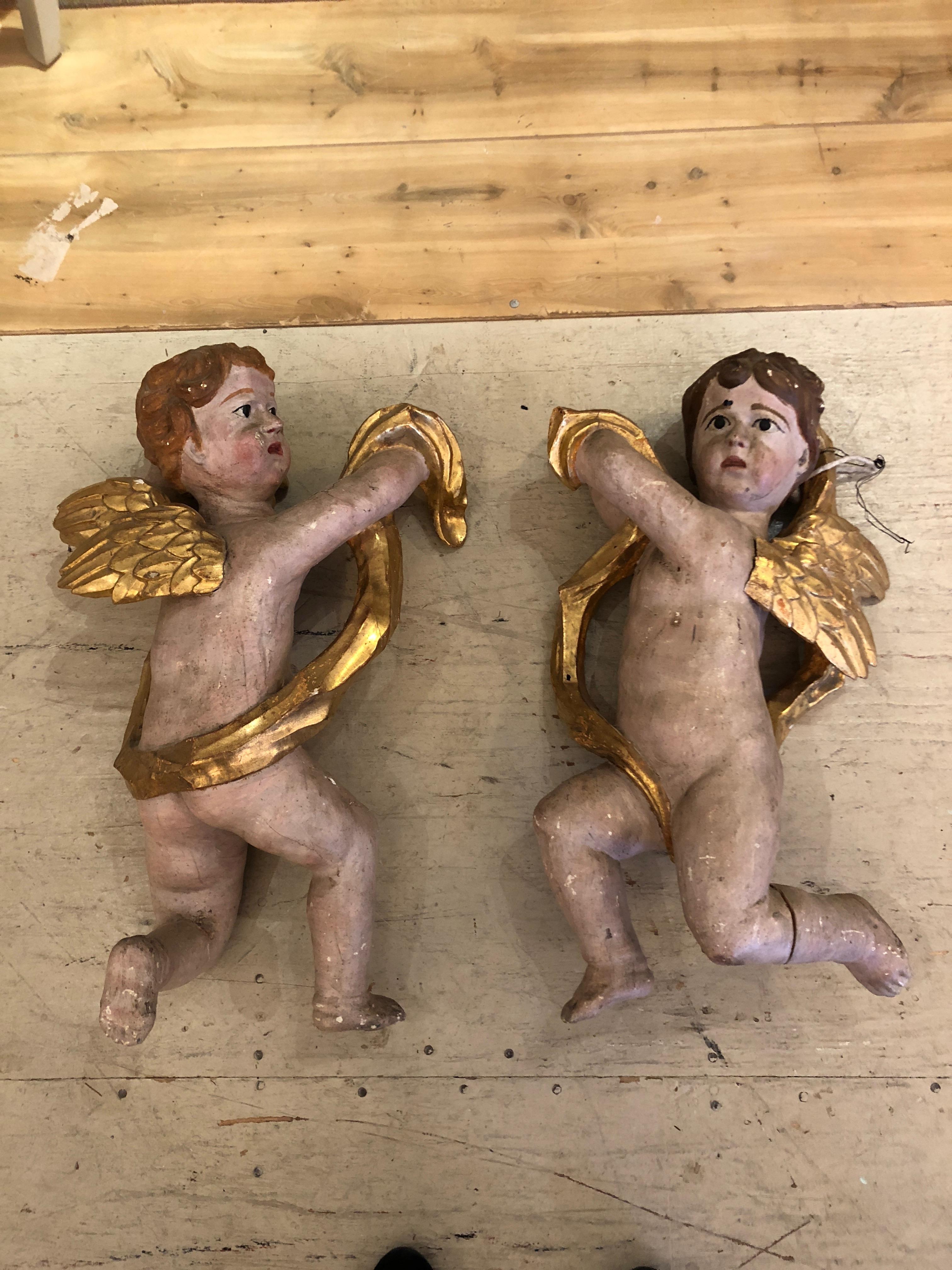 Wonderful very old pair of carved wood hand painted cherubs having gilded drapes, detailed wings and quizzical expressions.