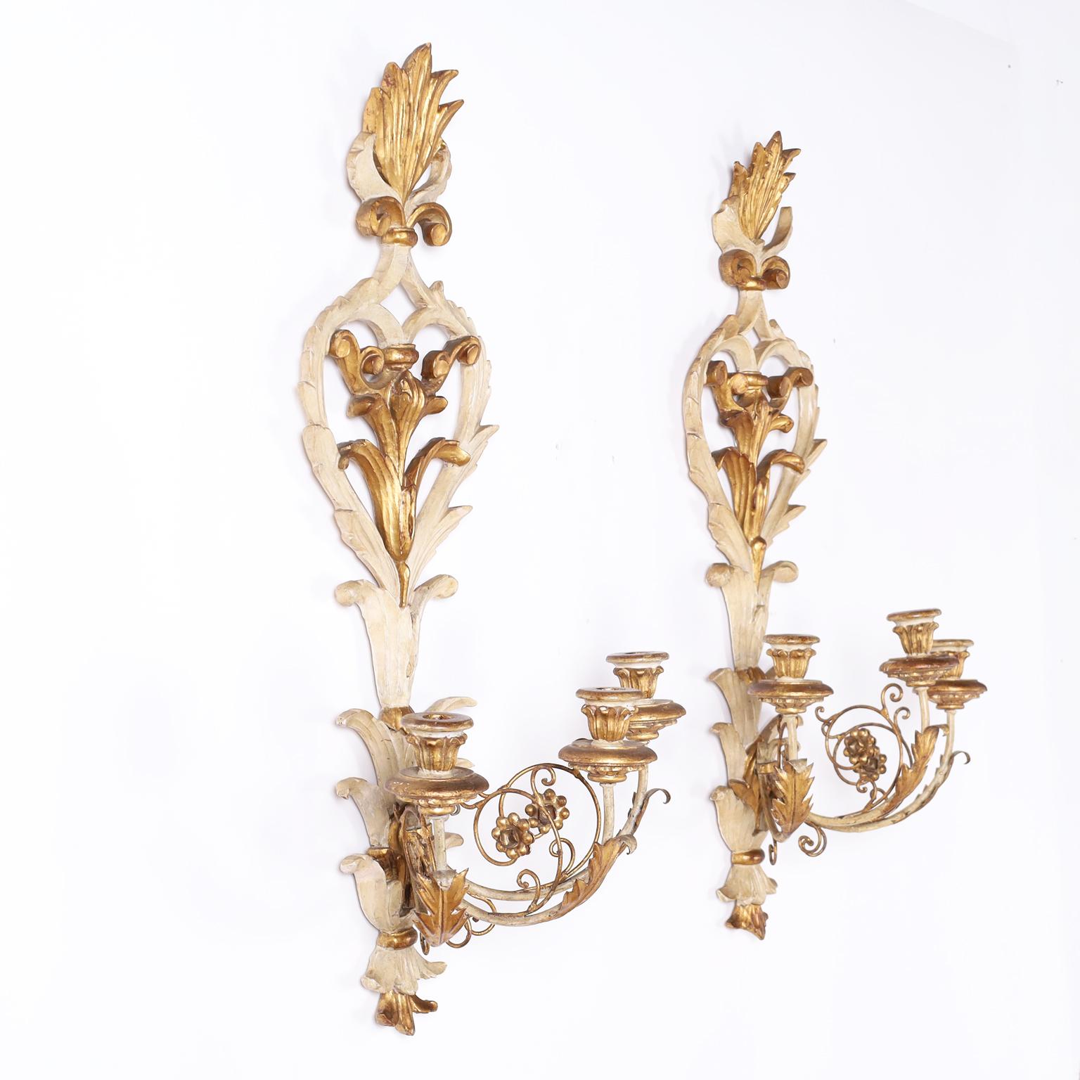 Pair of Italian sconces expertly carved with the original aged paint and gilt highlights, having a flame at the top and acanthus leaves over three metal arms with acanthus leaves and floral designs supporting carved candle cups.
   