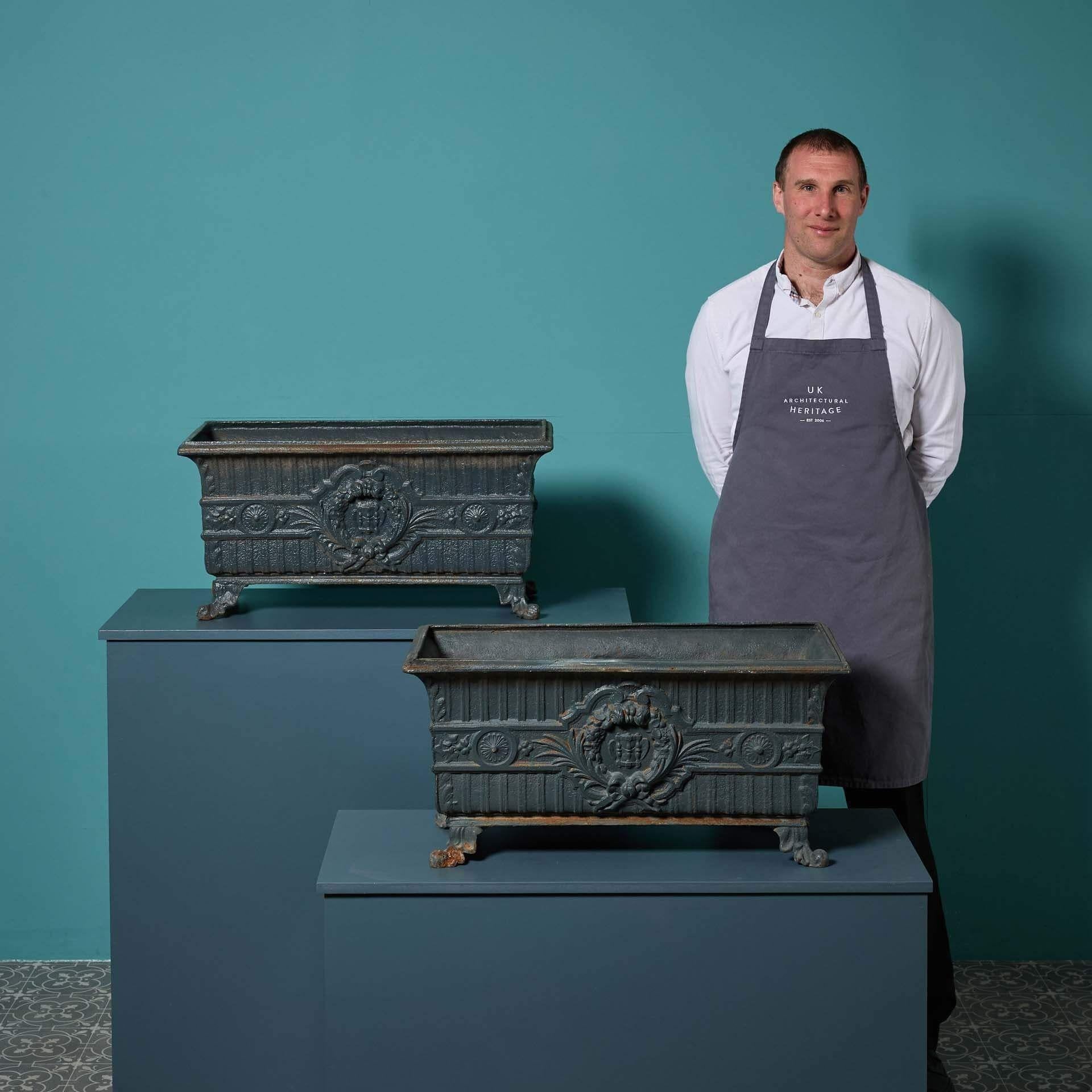Two antique cast iron trough planters of French origin, circa 1870. These beautiful matching trough plant pots are each of a spacious rectangular form with flared sides and scroll feet, the body ornamented with central cartouche to both
