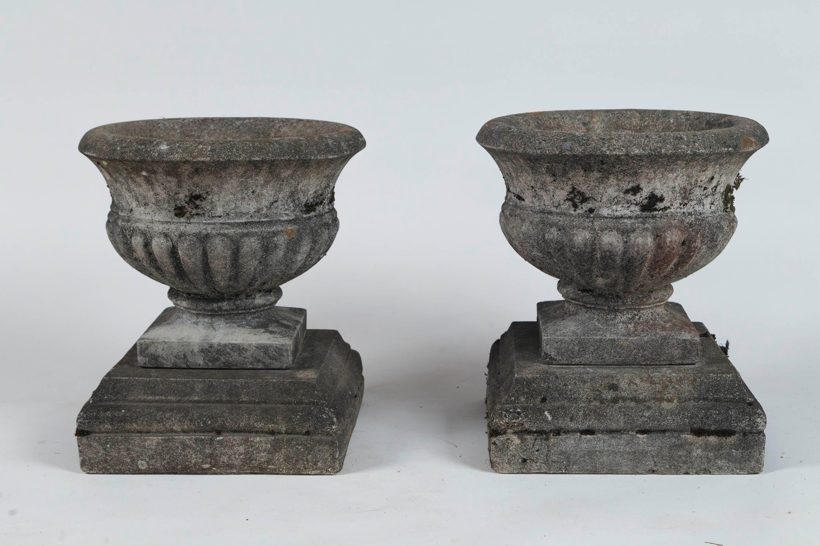 Pair of antique cast stone garden urns on bases, circa 1920. Tazza form urns with wonderful, weathered patina from a New England estate.