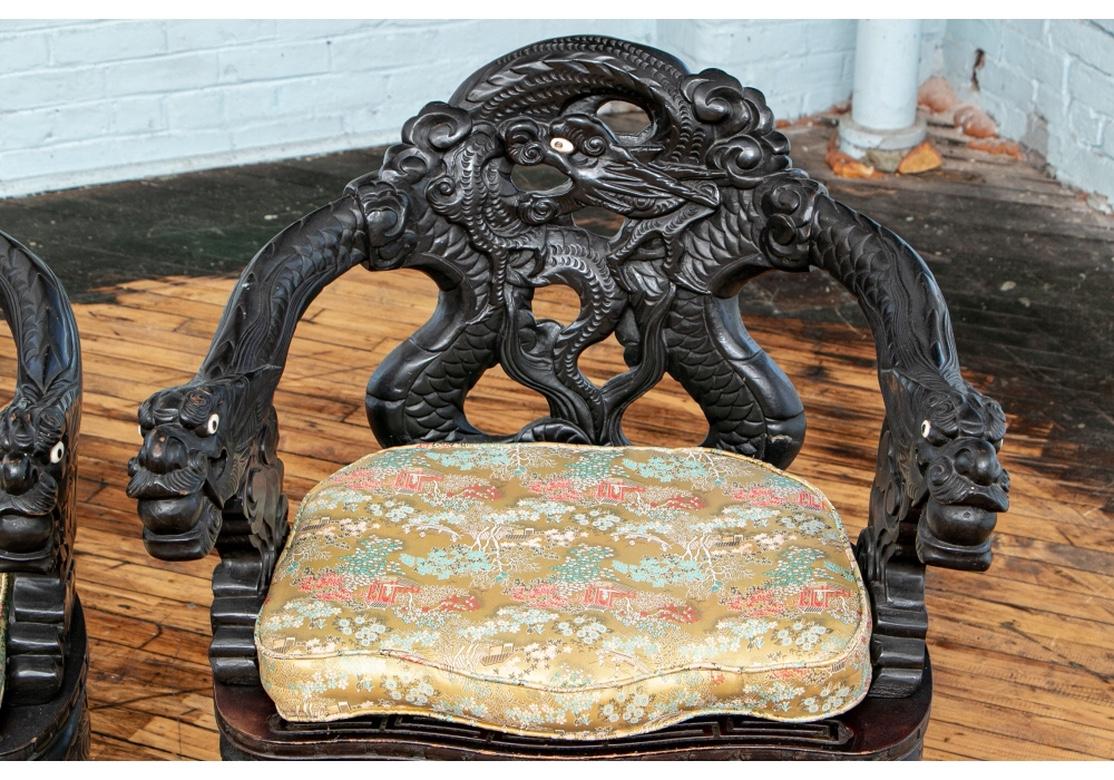 Elaborately carved and ebonized Chinese dragon thrones with openwork tub backs each with a dragon head, the curved scaly arms ending in dragon heads having bone eyes with balls in their mouths. The carved skirt raised on curved carved legs. The