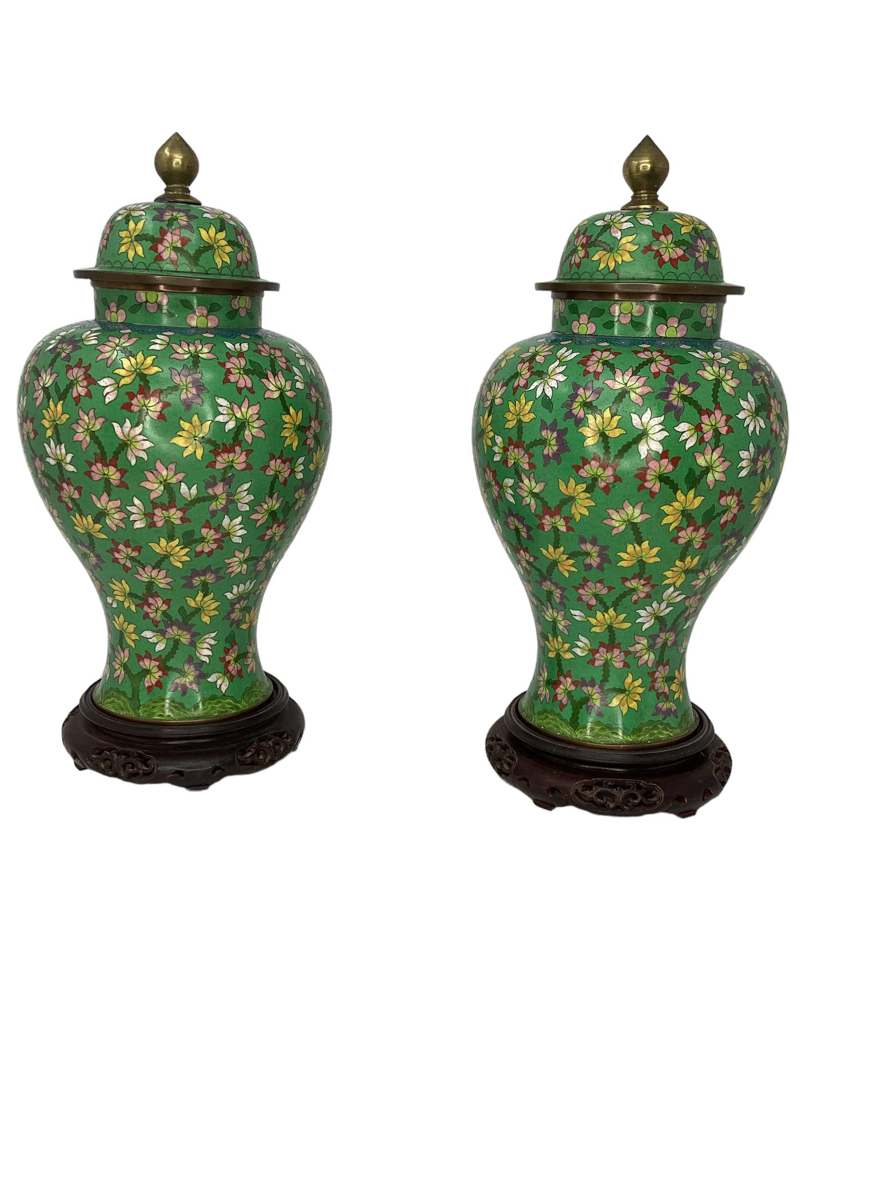 Pair of Antique Chinese Cloisonné Covered Ginger Jar Vases. Each with colorful floral decoration. The covers both have an acorn shaped bronze finials. Both on original carved hardwood bases. Stamped on the underside 