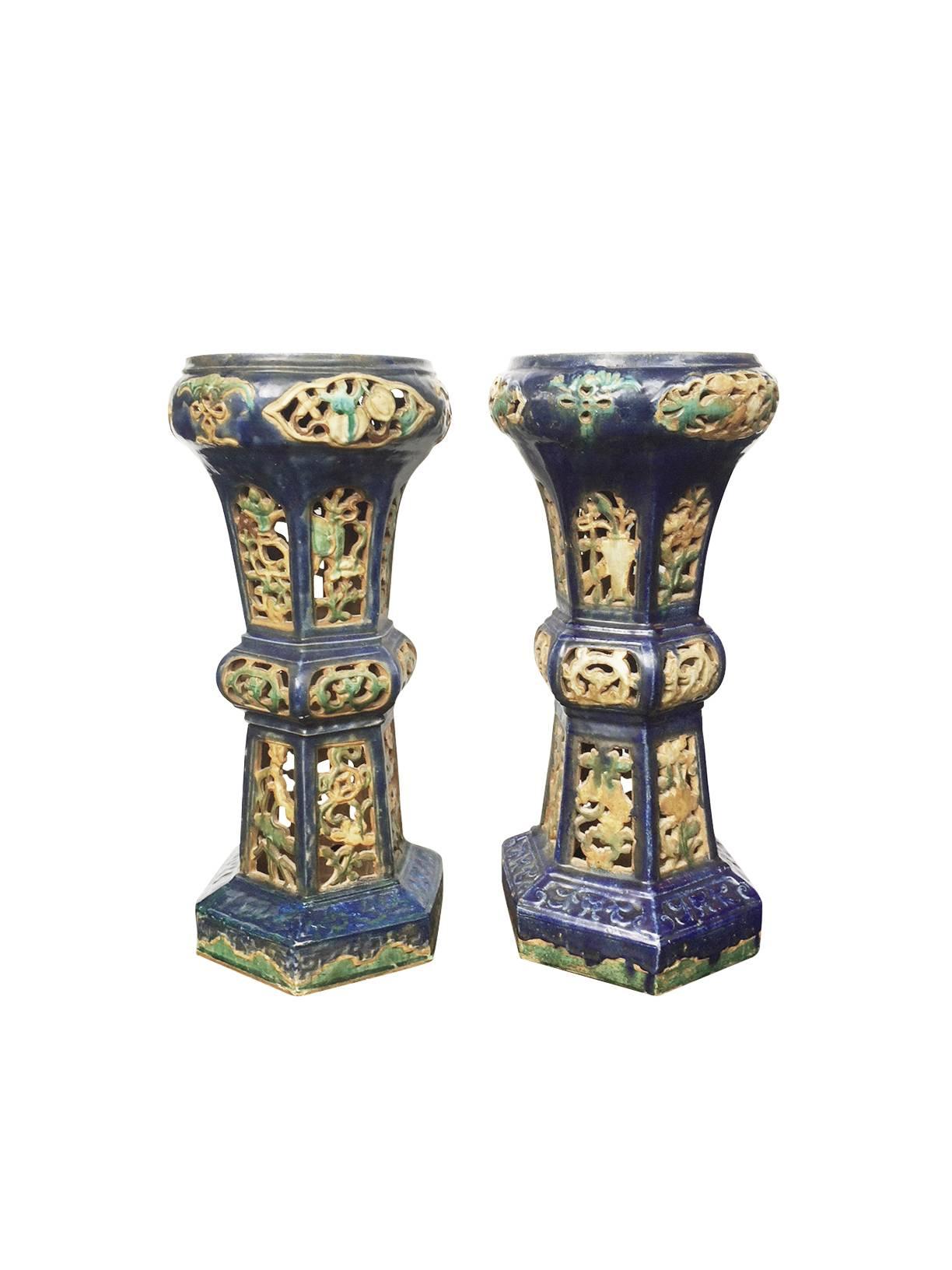 These two decorative ink-blue pedestals or end tables are antique and come from China. They are ceramic with a glaze that has slightly become matte and beautifully weathered over the years. Their design is floral with a trellis-like openwork