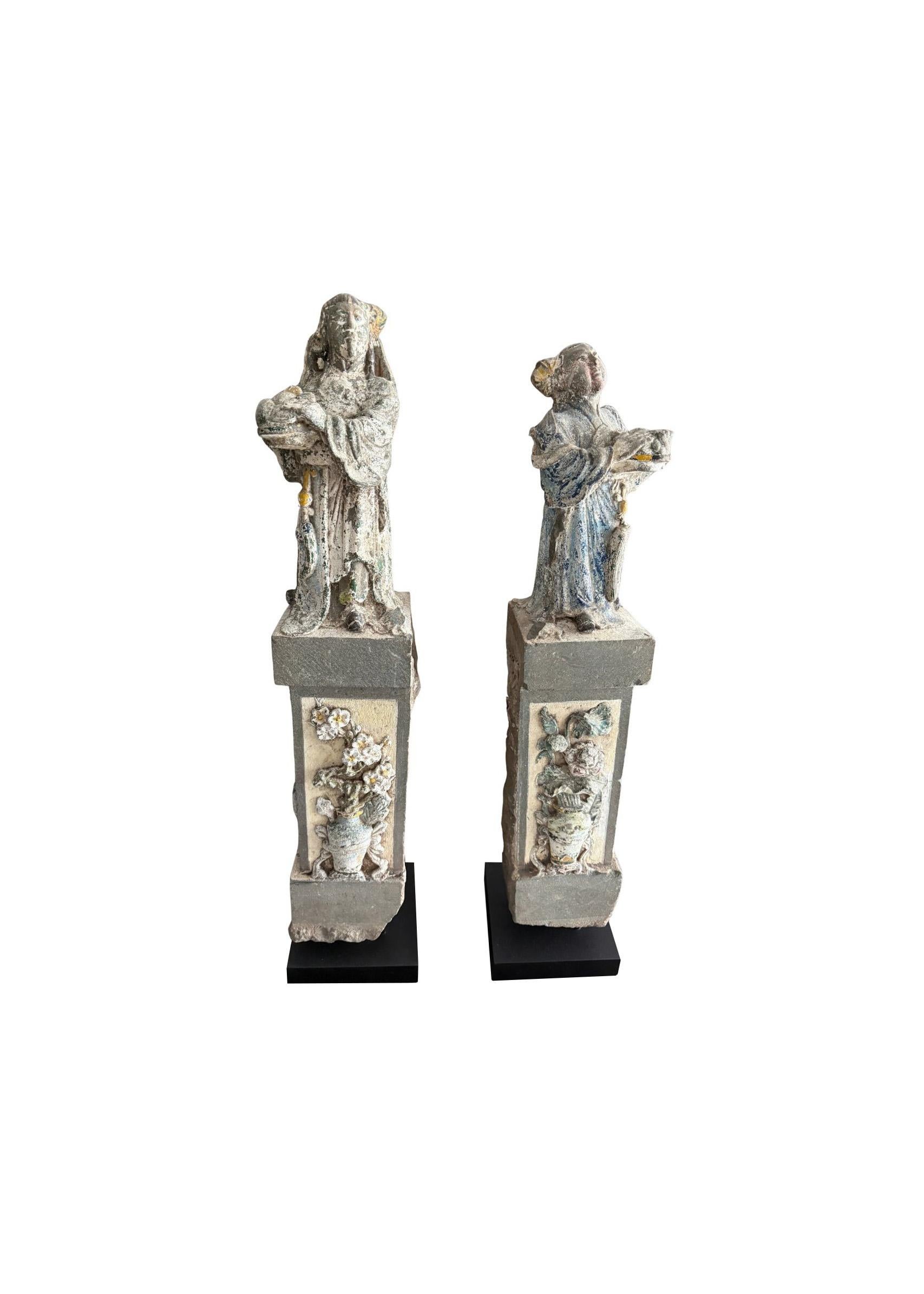 Cette étonnante paire de sculptures chinoises anciennes en granit présente des figures masculines et féminines finement sculptées, vêtues de robes traditionnelles, chacune se tenant sur un piédestal rectangulaire orné de reliefs floraux. Datant de