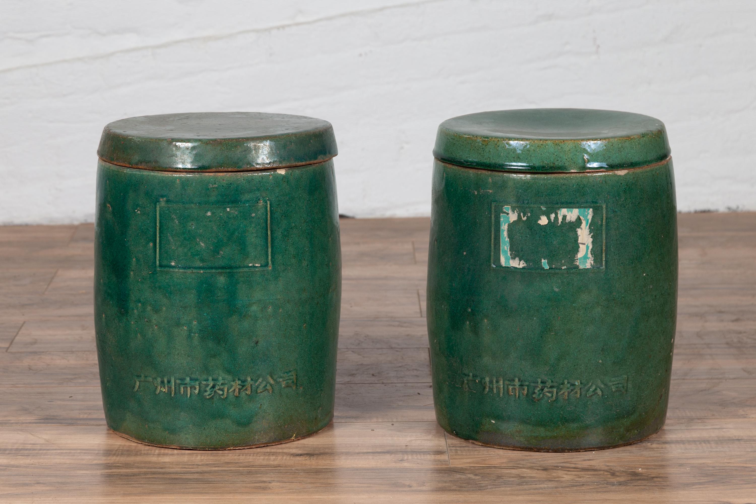 A pair of Chinese Hunan antique green glazed ceramic jars from the early 20th century, with lids and calligraphy. Born in the mountainous province of Hunan in southern China, each of this pair of green glazed lidded jars, features a circular body,