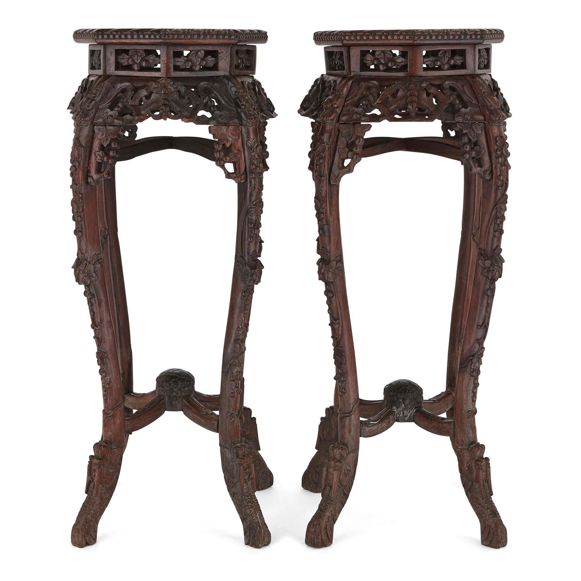 The stands in this matching pair are made from 'Hongmu' wood (Chinese hardwood). Each stand rests upon four stylised and flared dragon feet, which extend into four ornately carved cabriole legs. The legs are connected by upper and lower stretchers,