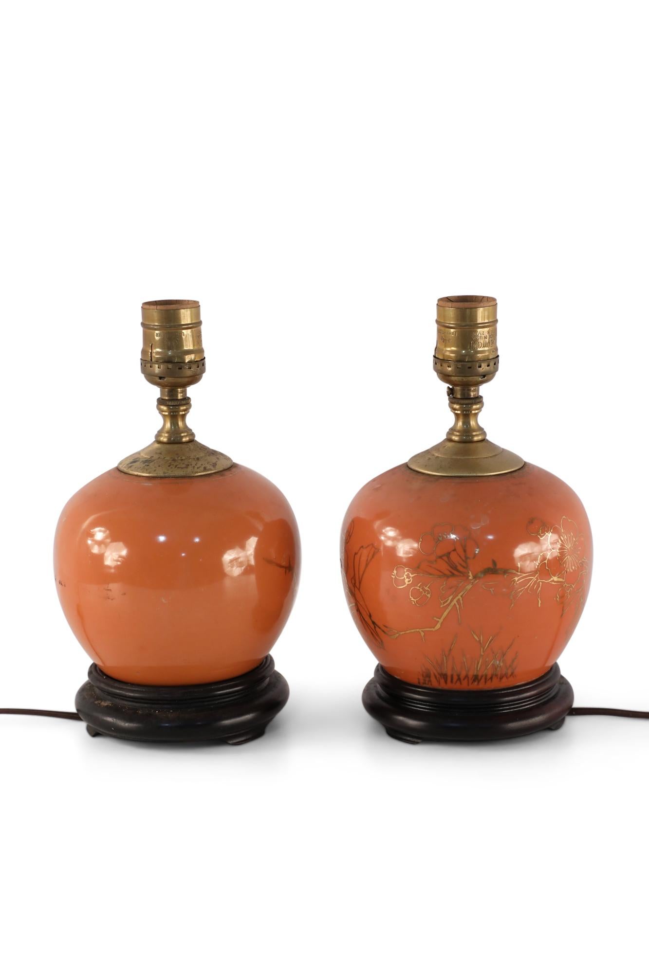Pair of antique Chinese (Early 20th Century) round table lamps made from orange, luster porcelain vases with gold floral designs, mounted on brown wooden bases with patinated brass hardware.