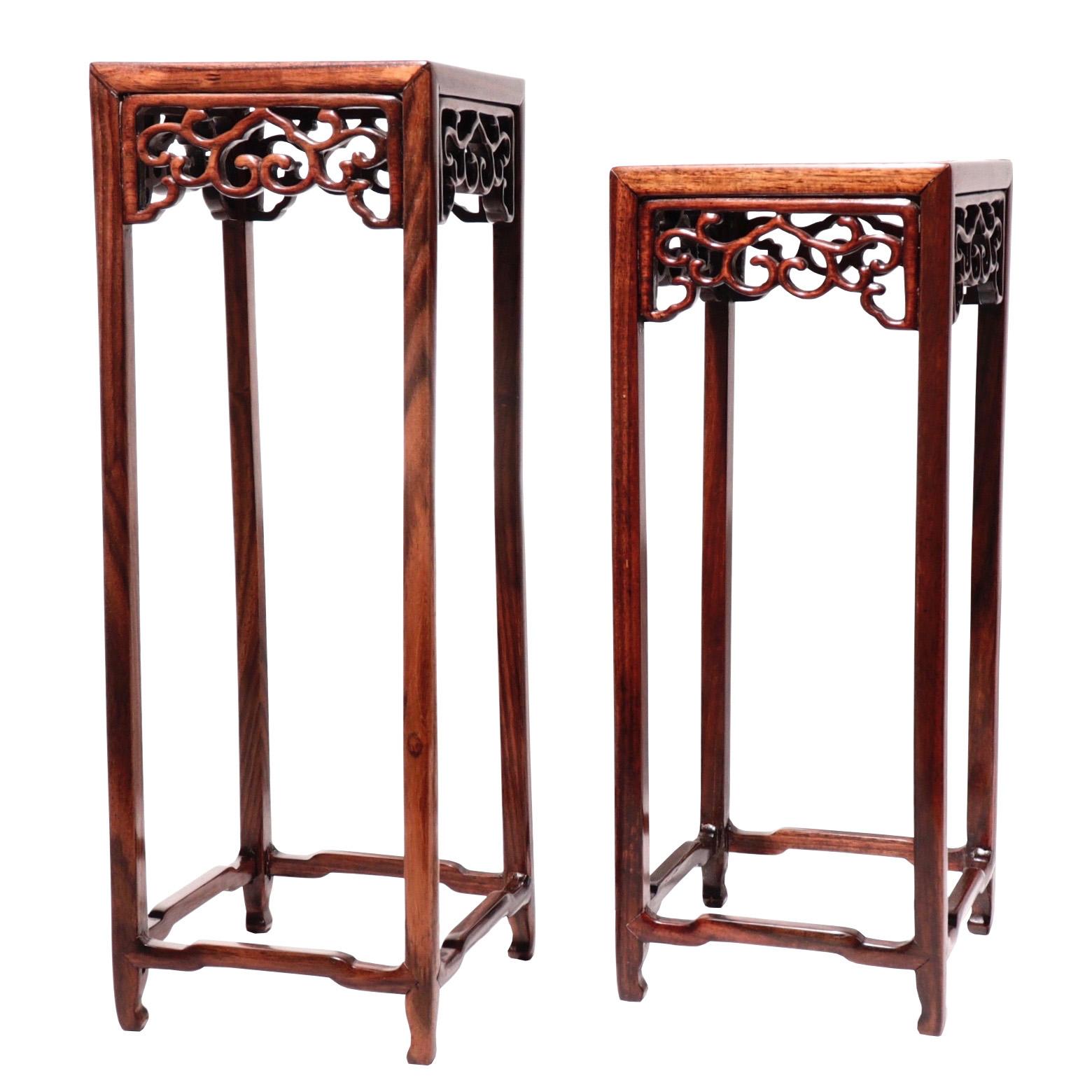 A set of two Chinese rosewood and burl wood curio display stands, in a tall pedestal form with thin legs and delicate pierced work apron in a ruyi vine design, elbowed cross stretchers near the base and center burl wood panel, varied in