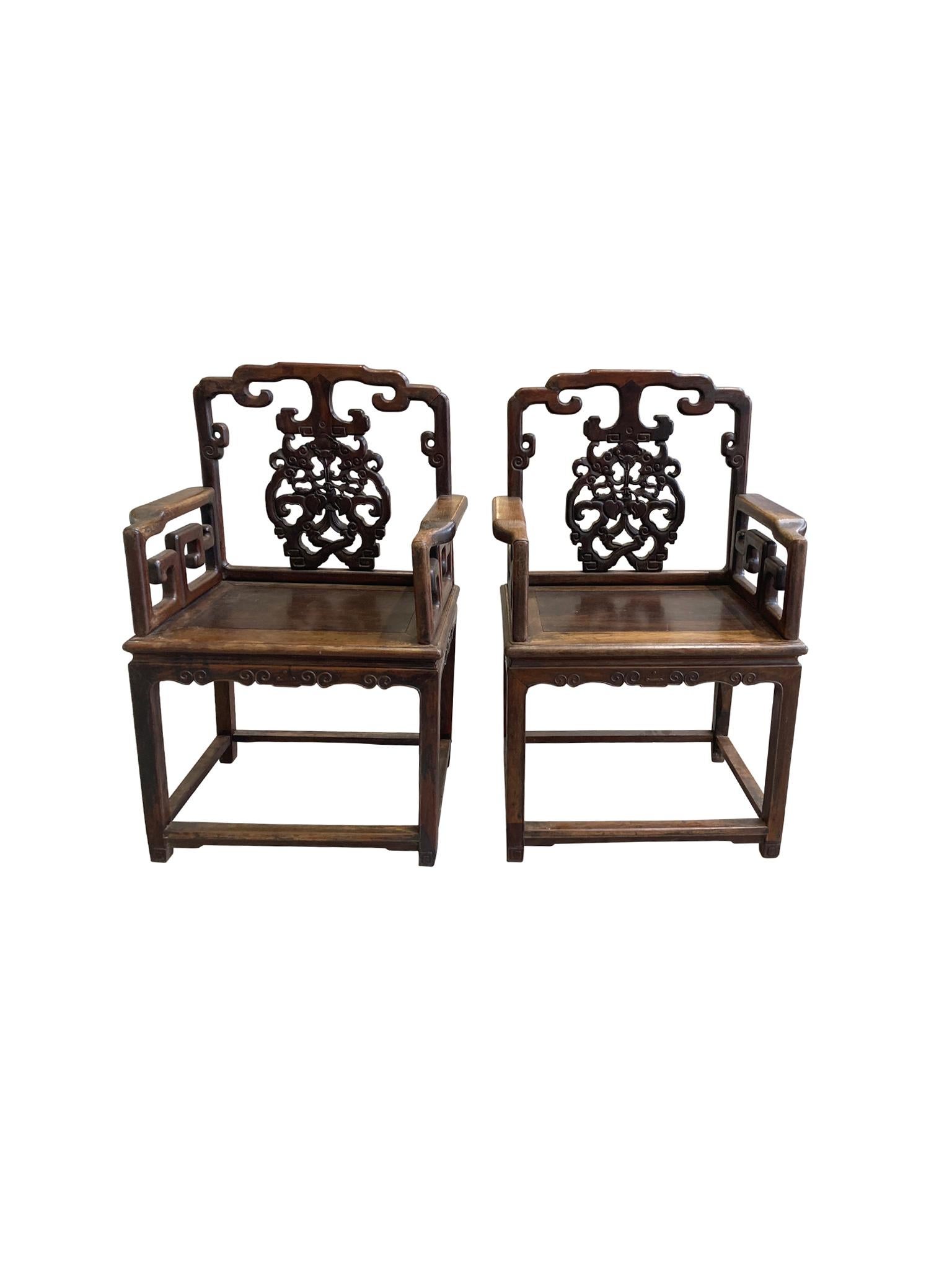 A pair of antique Chinese armchairs crafted from rosewood, possibly Huanghuali rosewood, circa Late 19th century. The back is decorated with hand carved fruit and fauna motifs. We love the combination of intricate swirling forms and the more squared