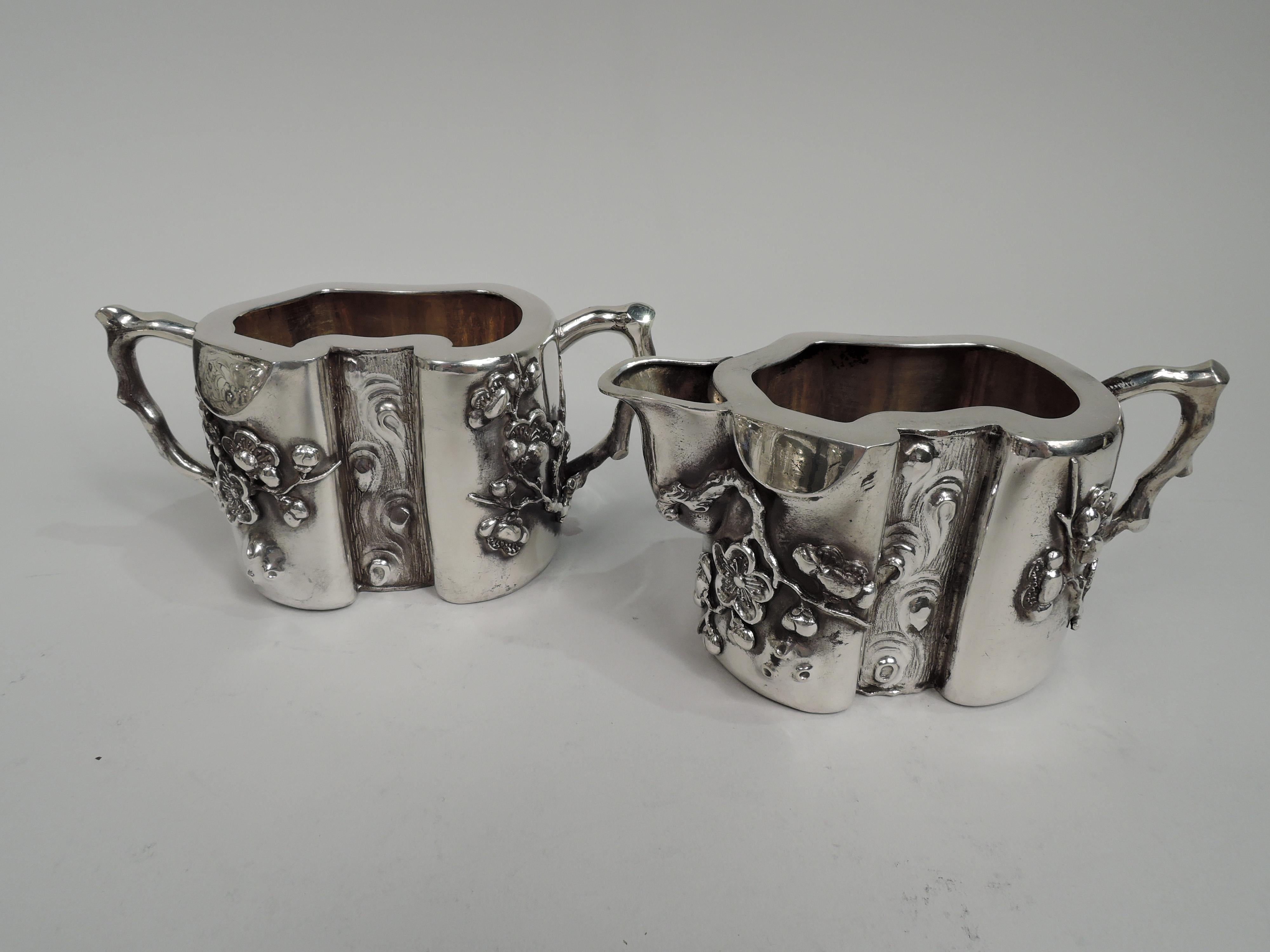 Pair of Chinese silver creamer and sugar, ca 1910. Each: Ovoid serpentine body. Center front inset with striated tree trunk and scrolling burls. Applied blossoming prunus branches. Handles twig form. Creamer has u-spout. Gilt-washed interior. Both