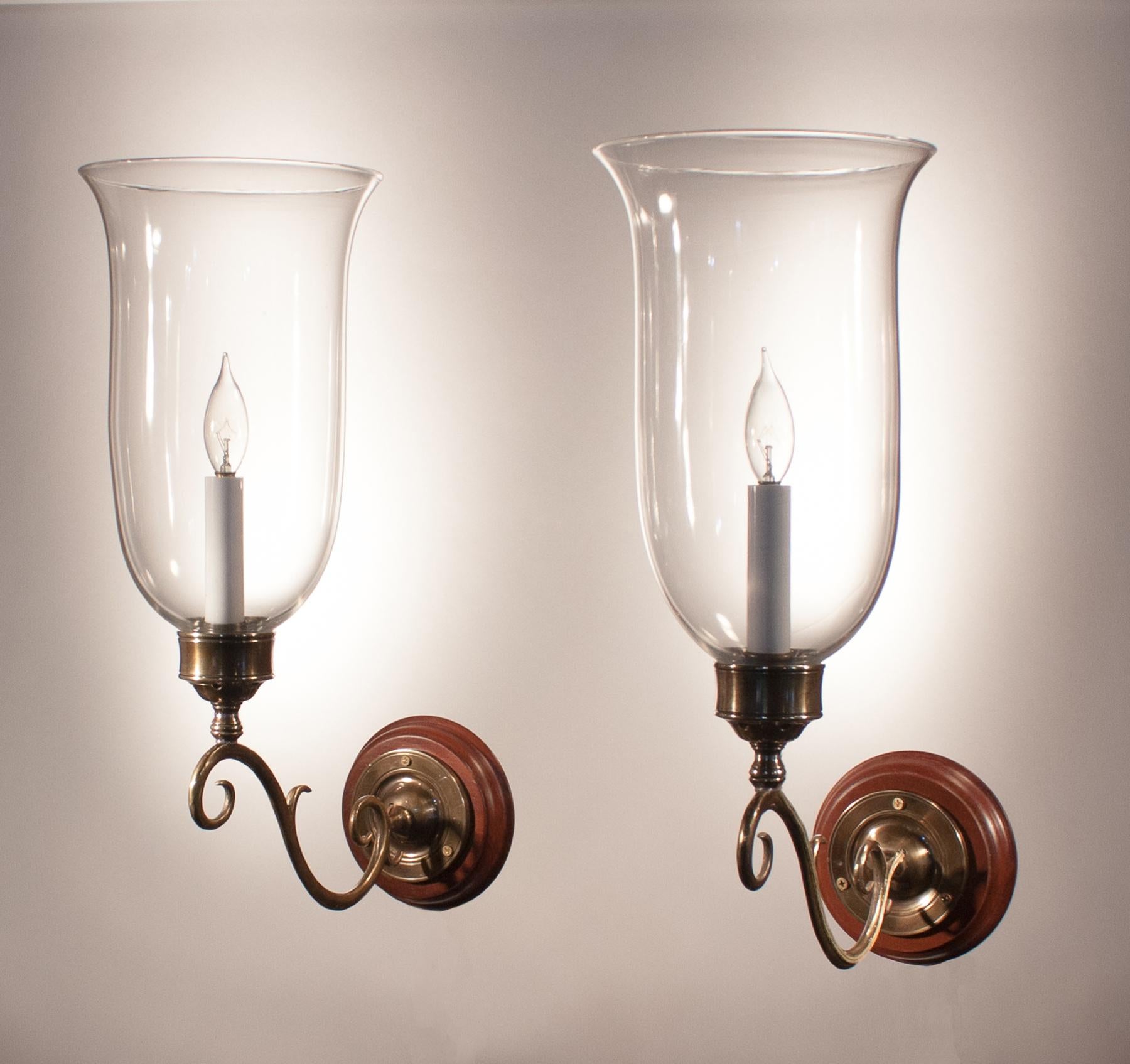 Pair of superb quality hand blown glass hurricane shades from England, circa 1890. These flared shades have classic form, and their proportion is well-suited to the scroll brass sconce arms. The custom-fabricated sconce arms and mahogany backplates