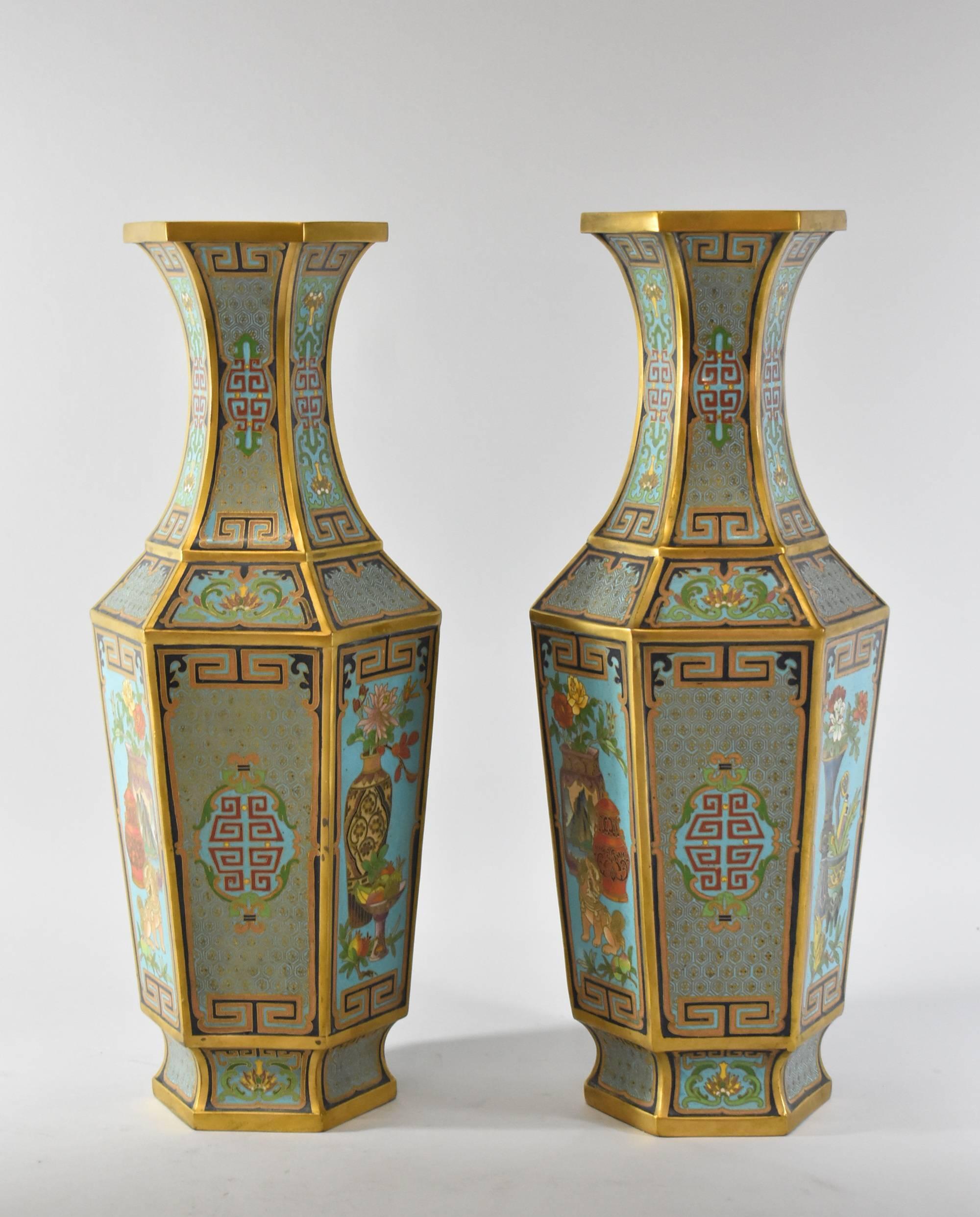 A gorgeous pair of cloisonné Vases. These stunning vases feature temple dog images, floral designs and fruit baskets in brilliant colors. They are six-sided, hexagon shaped, with a turquoise interior and bottom. They are marked #21 on the bottom.