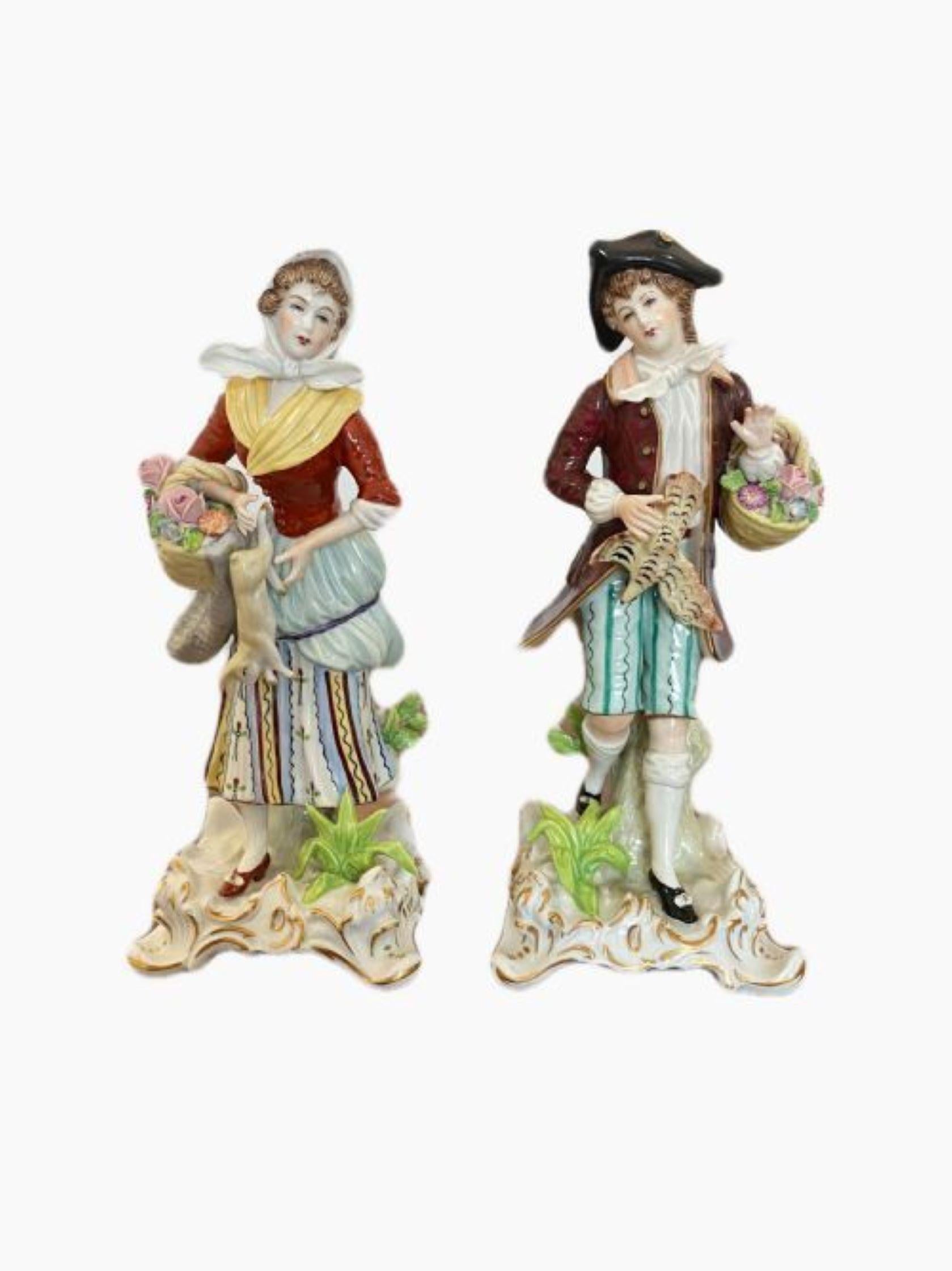 Pair of antique porcelain figures holding a basket of flowers in wonderful colourful period clothing in red, yellow, green and blue colours standing on a shaped base with gilded scrolls