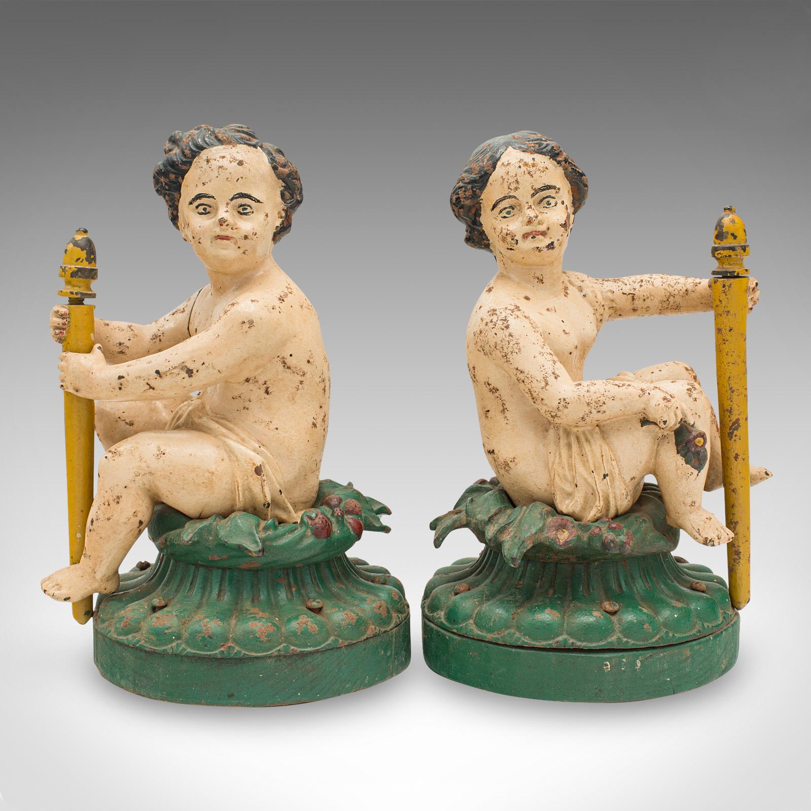 This is a pair of antique decorative figures. An English, painted cast iron putto on elm base, dating to the Victorian period, circa 1870.

Delightfully unusual figures with Rubenesque appeal
Displaying a desirably aged patina throughout
Substantial