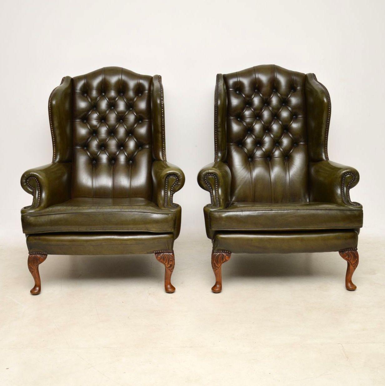 Large pair of antique leather wing armchairs with hump backs, shaped wings, deep buttoned backs and well carved walnut legs. These armchairs are very comfortable with plenty of back support. The green leather is naturally aged and has been polished,