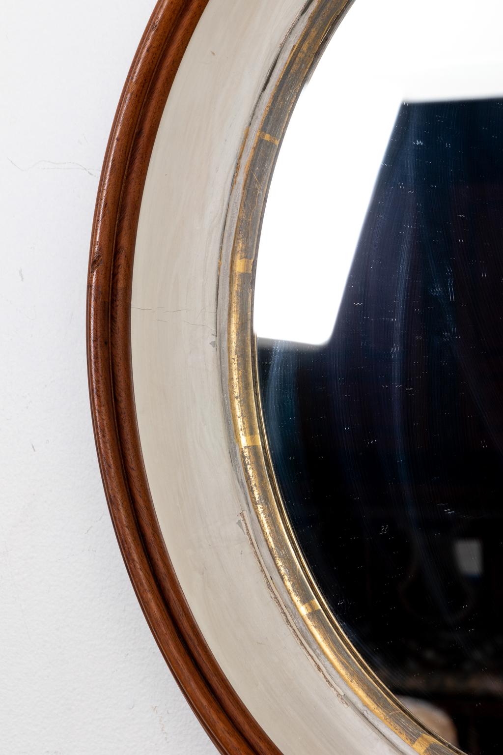 Circa 1920s pair of antique deep set oval mirrors featuring wood in a stained, painted, and gilt finish. Made in the United States. Please note of wear consistent with age.