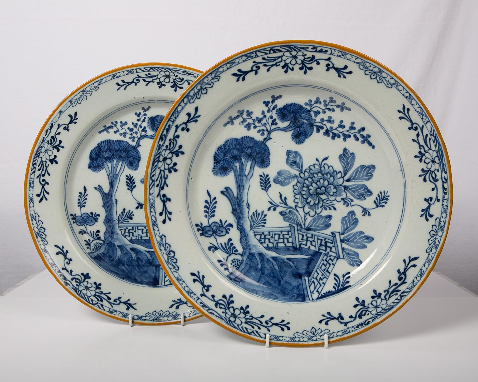 A pair of antique Blue and White Dutch delft chargers made in the 18th century circa 1780. The centre is painted in shades of soft cobalt blue showing a garden scene with a deep rooted pine tree, a large peony, and a garden fence. The Dutch potter