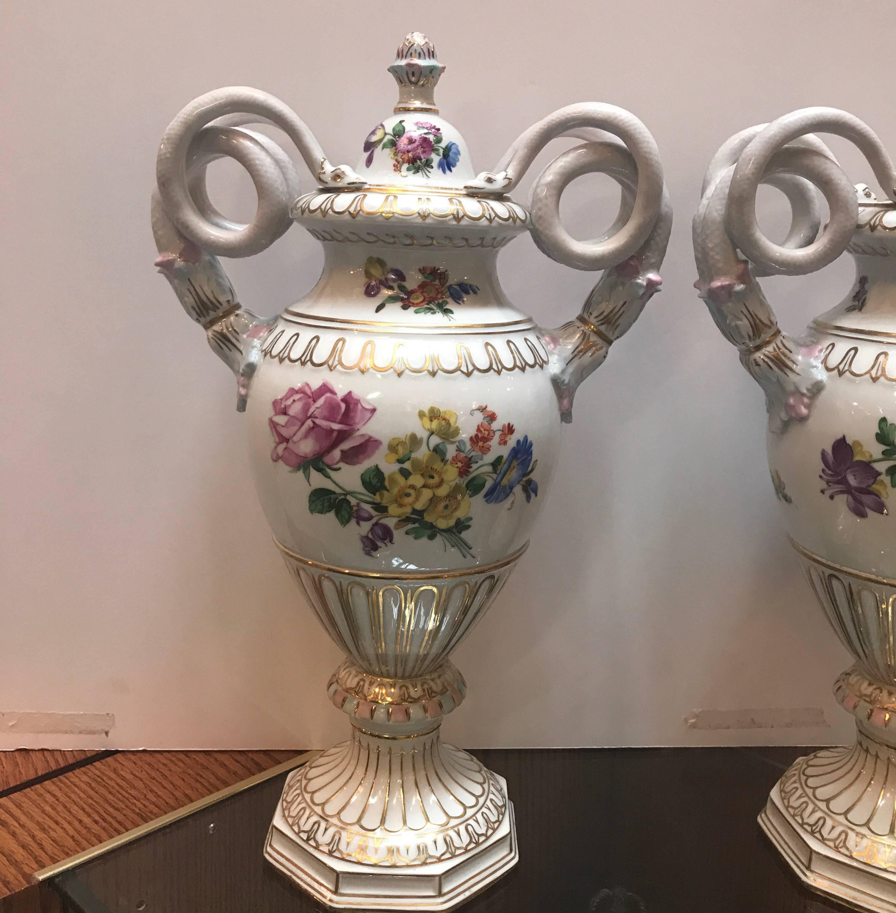A pair of hand-painted porcelain urns with a Dresden mark. The lidded urns with classic snake handles with gilt decoration all over. The centers with hand-painted Dresden floral bouquets on both sides. The mark is the registered mark for Dresden