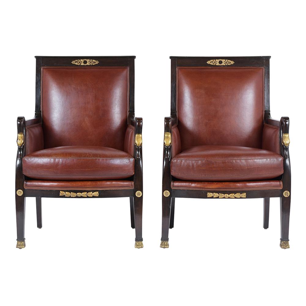 This pair of Antique Ebonized Empire Leather Lounge Chairs are made out of mahogany wood stained in an ebonized color with a beautifully polished patina finish and has been newly restored. The armchairs feature brass accents throughout the piece, a