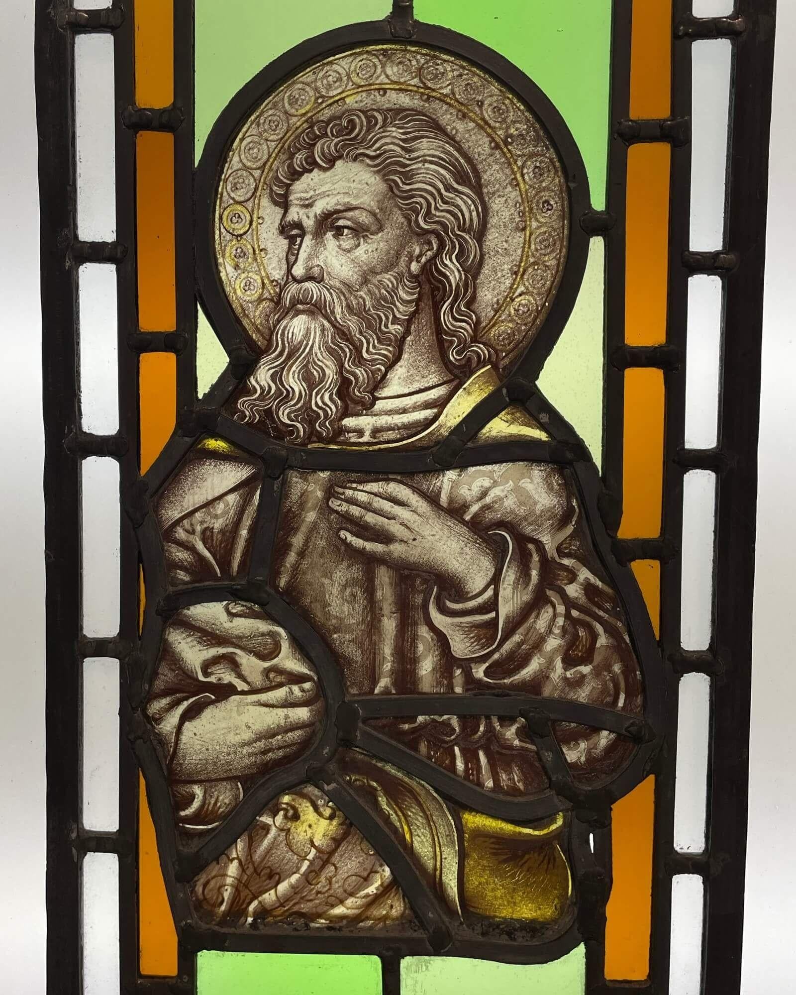 A pair of antique ecclesiastical stained glass windows circa 1850 depicting two saintly figures: one a bearded, long-haired man and the other a young boy with locks of blonde hair. Each is set into a backdrop of vibrant green and orange glass,