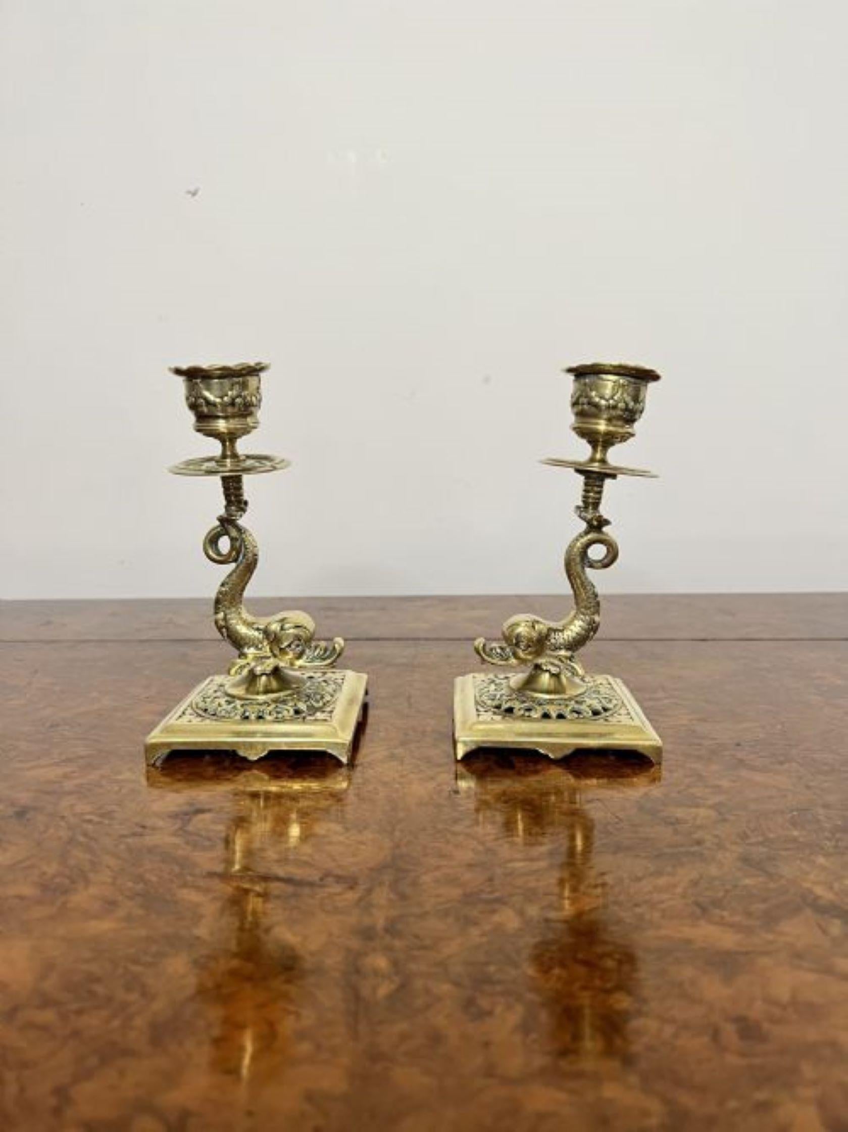 Pair of antique Edwardian quality unusual brass candlesticks having a quality pair of antique Edwardian ornate brass candlesticks with unusual dolphin supports on a square ornate brass base.