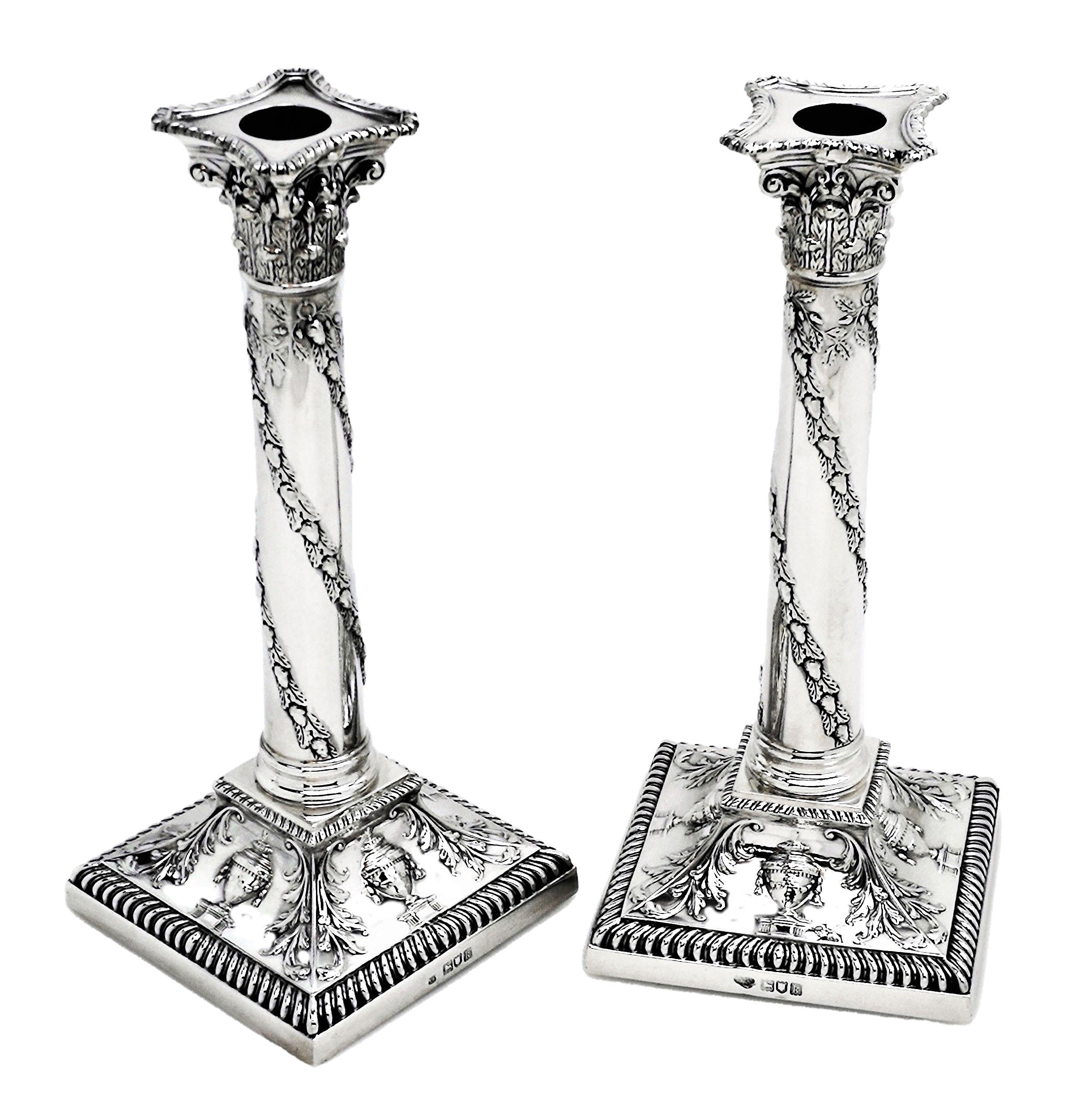 A pair of Antique Sterling Silver Candlesticks with acanthus leaf covered classic Corinthian style capitals above a column wrapped in acorn covered vines. The base of the Candlesticks feature a concave shape embellished with classical urns