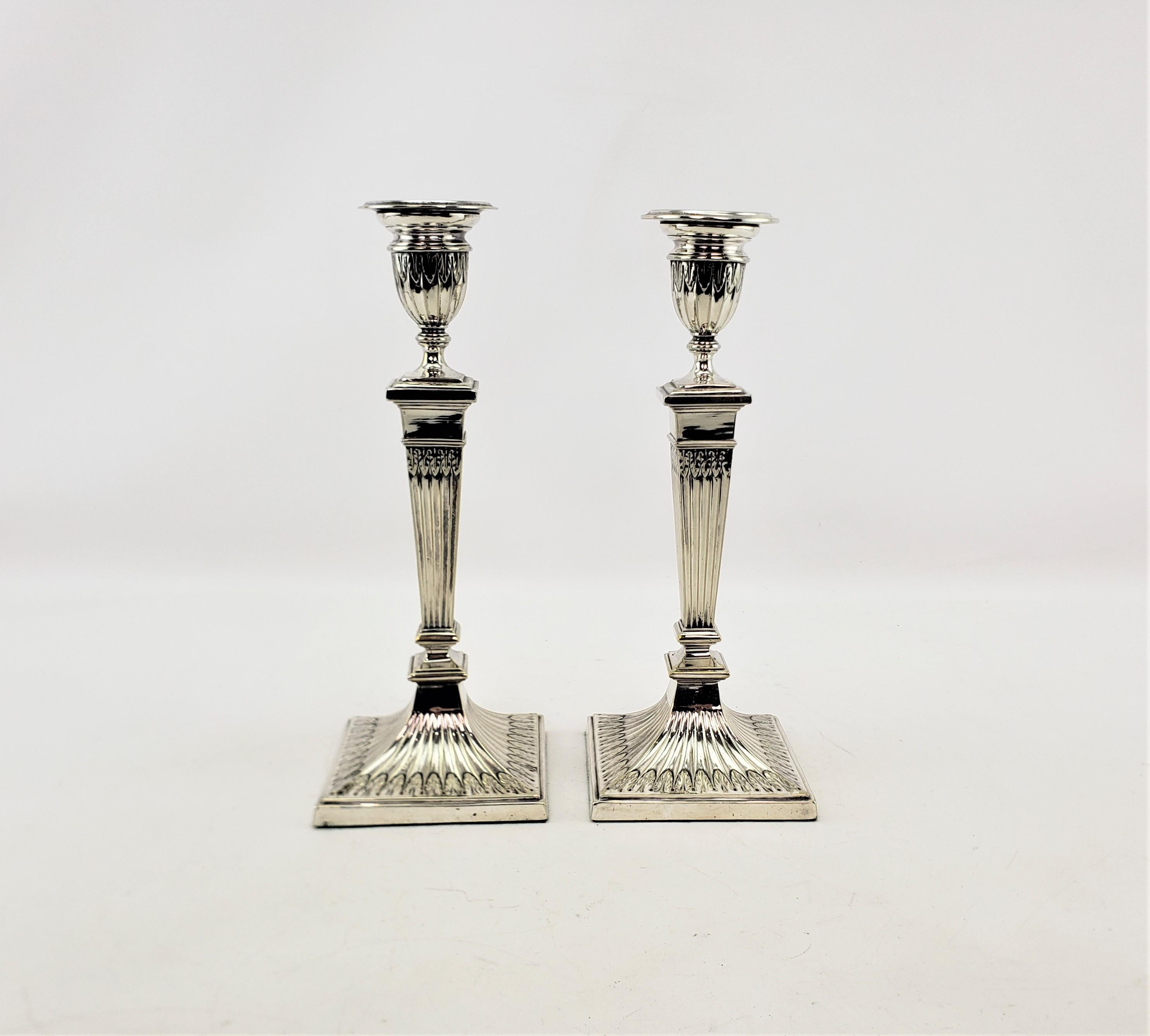 Questa coppia di candelieri antichi è stata realizzata dalla nota azienda inglese Elkington nel 1920 circa, in stile Art Deco. I caldestrelli sono composti da una lastra d'argento e presentano una decorazione a foglie stilizzate intorno ai lati