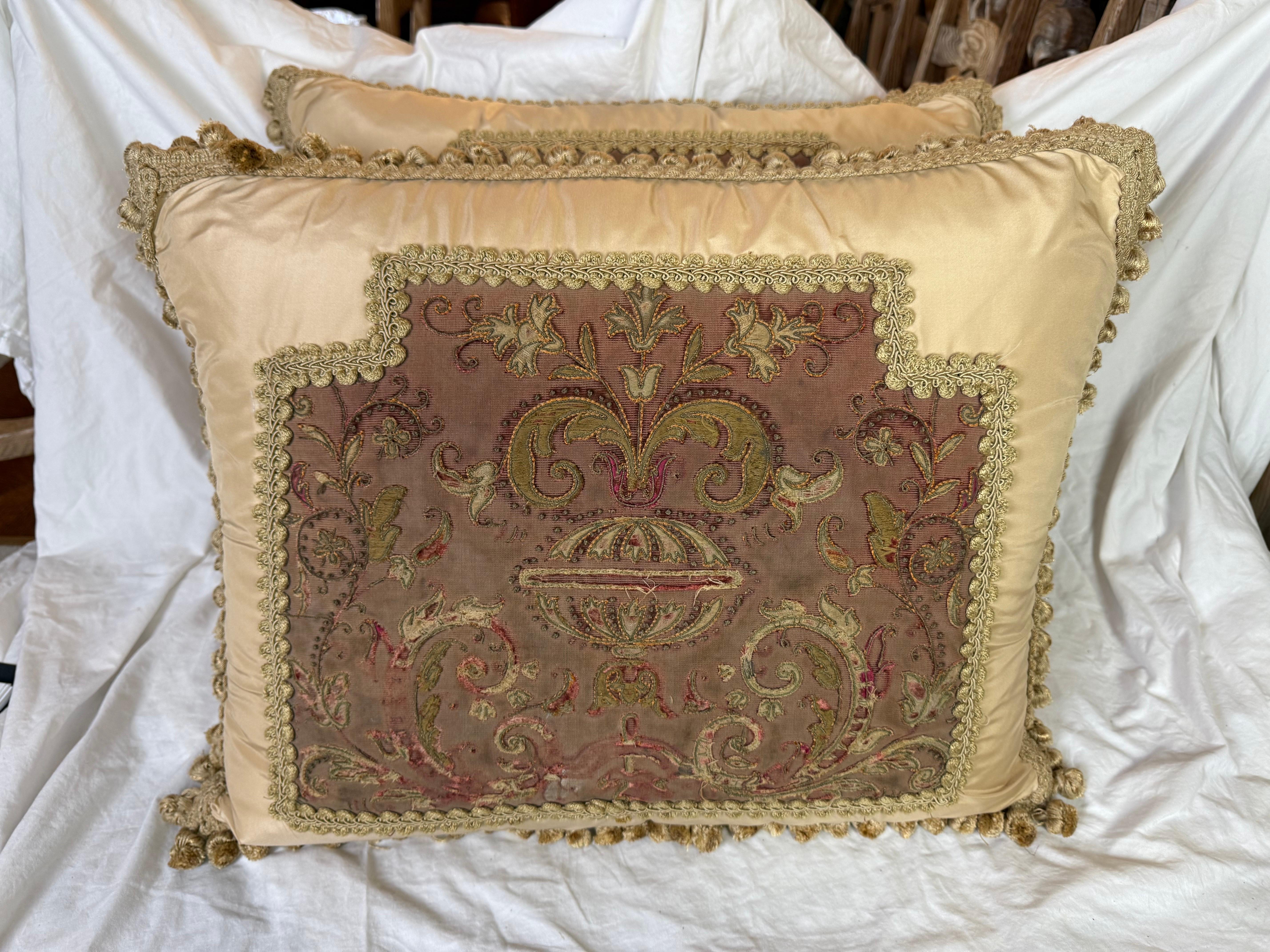 Ces élégants coussins allient admirablement l'art textile historique au luxe contemporain. La pièce maîtresse de chaque oreiller est un panneau français brodé du XIXe siècle, présentant un motif élaboré de feuilles d'acanthe enroulées, de motifs