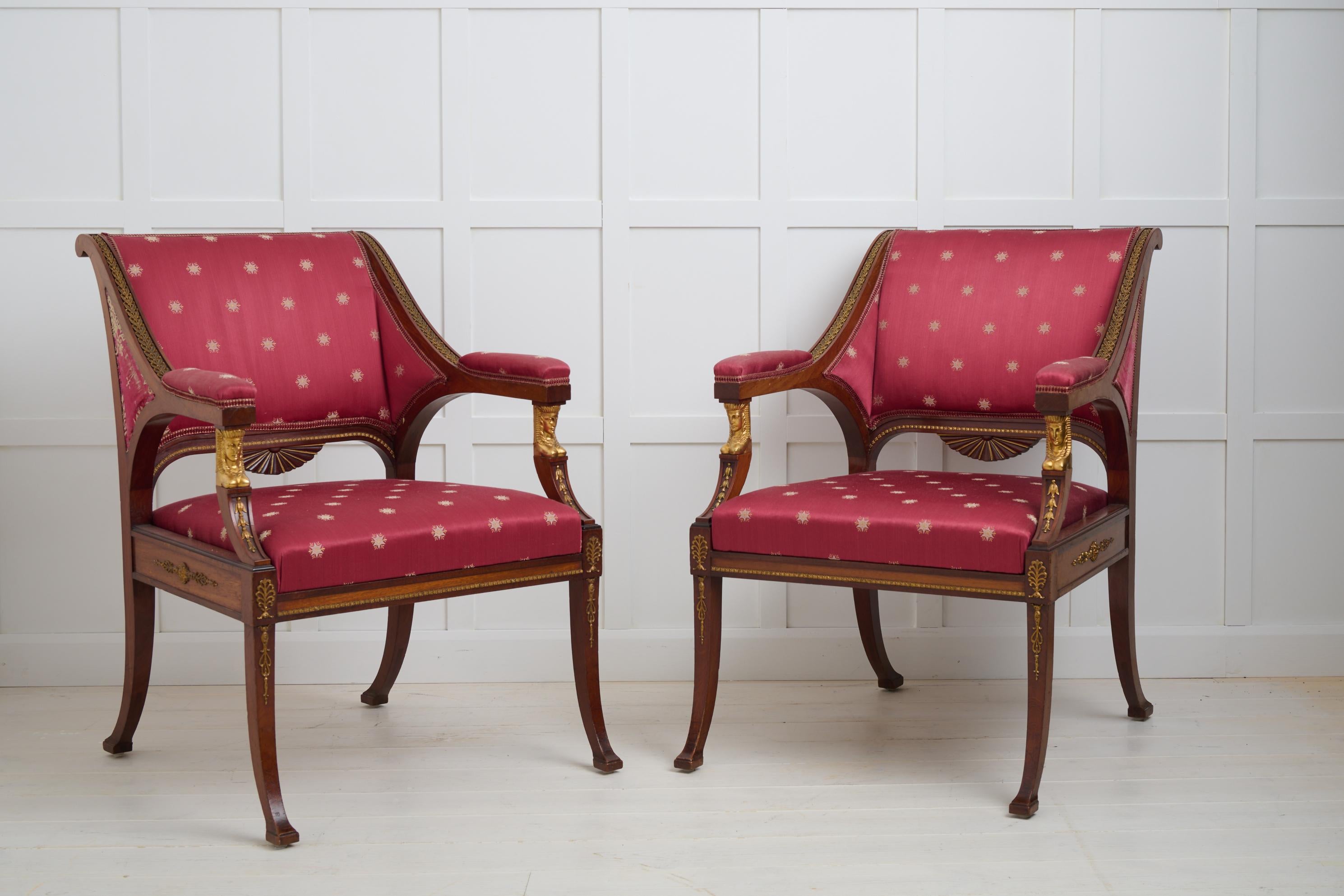 Pair of Swedish empire armchairs with a frame in mahogany made around 1830 to 1840. The chairs have decorative elements in brass, glided Egyptianized sphinx heads in the armrests and curved saber legs. Good vintage condition with smaller marks and