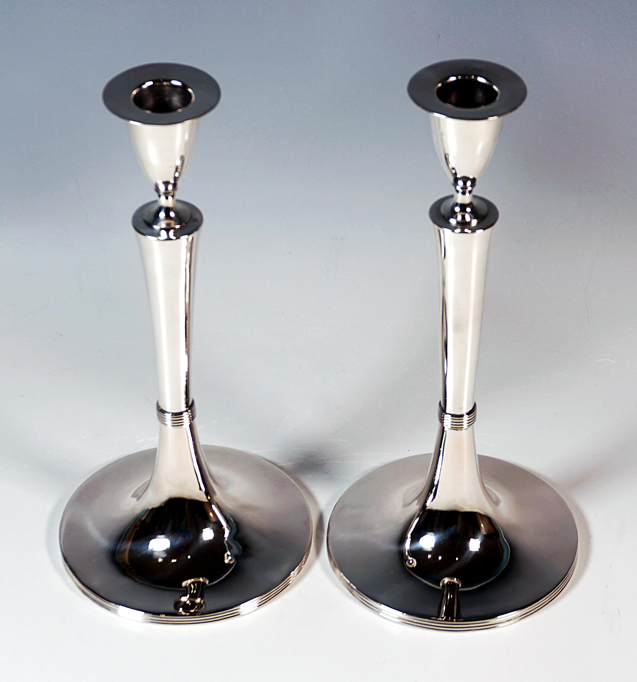 Due eleganti portacandele d'argento liscio su un supporto rotondo, piede profilato lateralmente, fusto liscio rialzato al centro, nel terzo inferiore costretto da un anello di perline profilato, fusto che si allarga conicamente verso l'alto, con