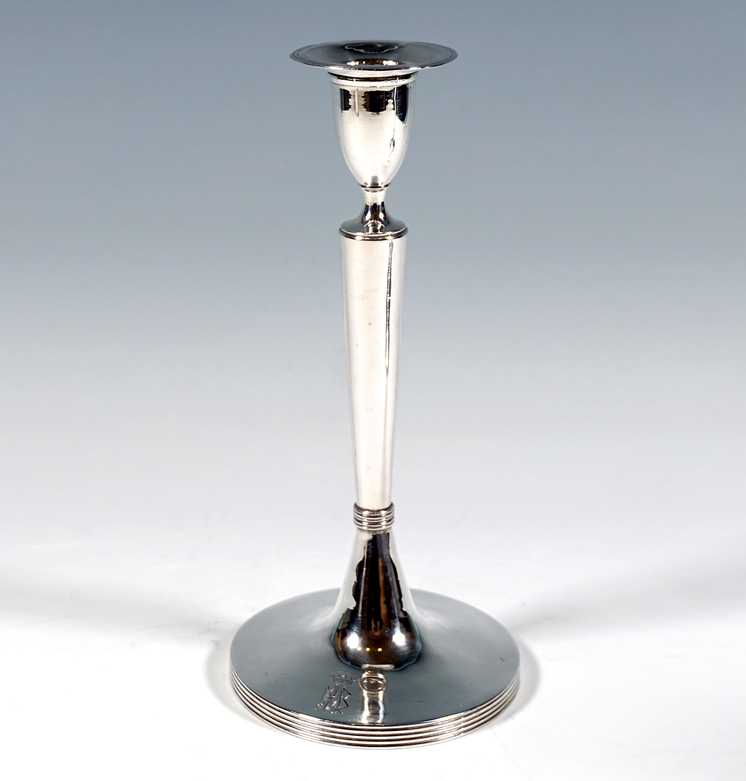 Due eleganti portacandele d'argento liscio su un supporto rotondo, piede profilato lateralmente, fusto liscio rialzato al centro, nel terzo inferiore costretto da un anello di perline profilato, fusto che si allarga conicamente verso l'alto, con