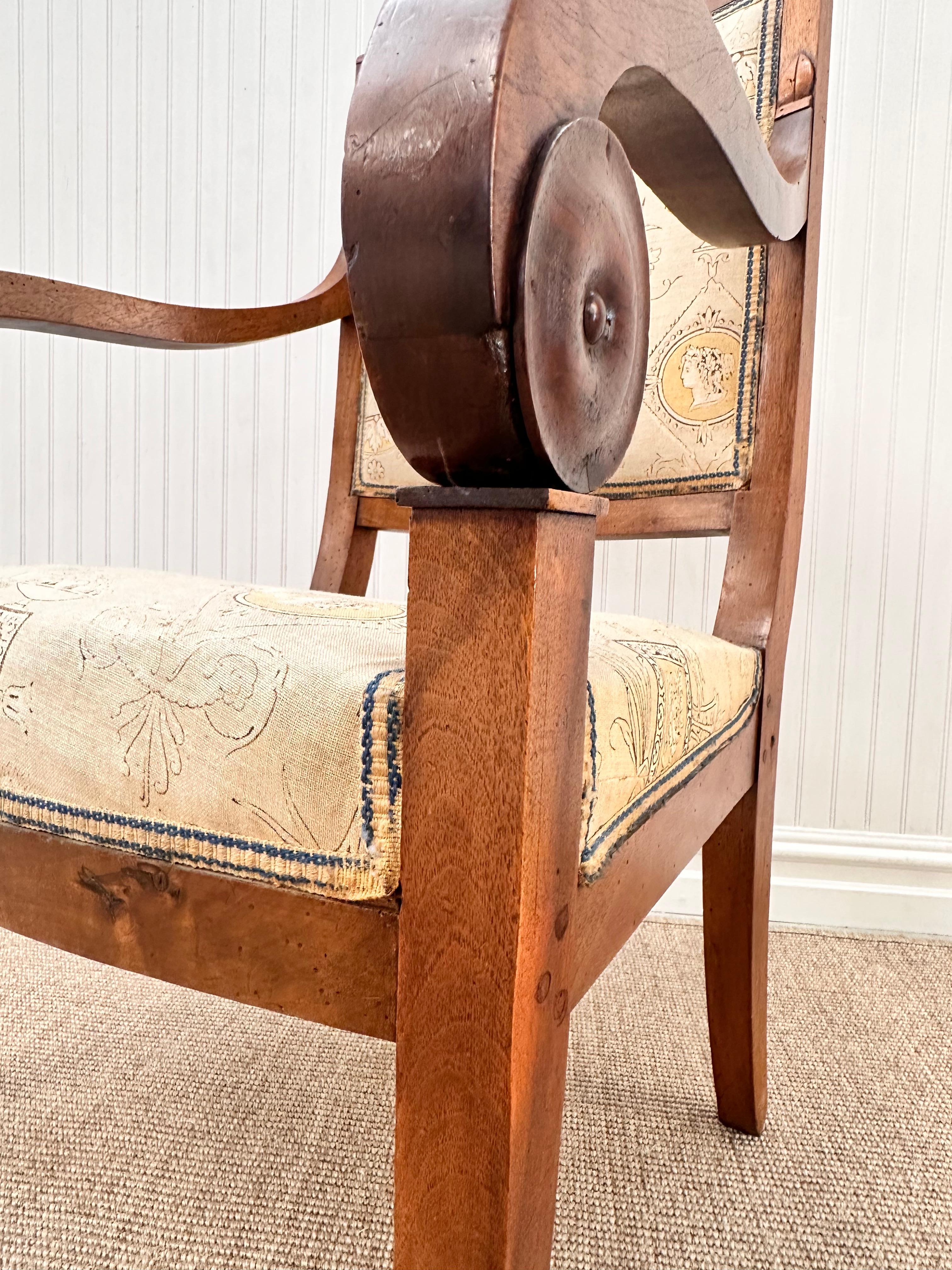 Es handelt sich um antike Sessel im Empire-Stil, die sich durch elegante Handwerkskunst und klassische Designelemente auszeichnen. Der Rahmen ist aus reichem, mitteltönigem Holz mit einer warmen, polierten Oberfläche gefertigt. Der Clou sind die