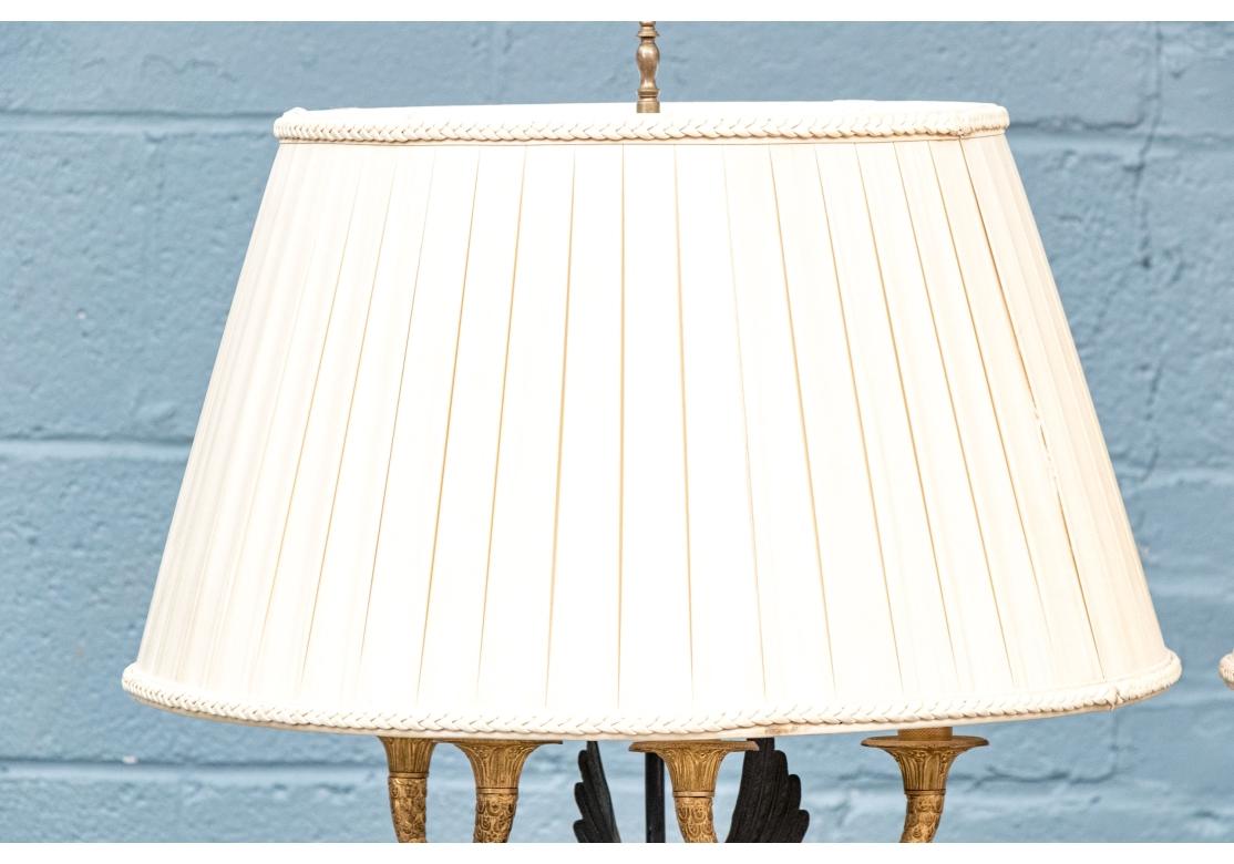 Finas lámparas de sobremesa con forma de candelabro de dos luces. Una figura negra de Victoria alada sostiene unos brazos en forma de doble cuerno dore con finos detalles y zócalos con velas de imitación de madera gris.  Está de pie sobre una bola
