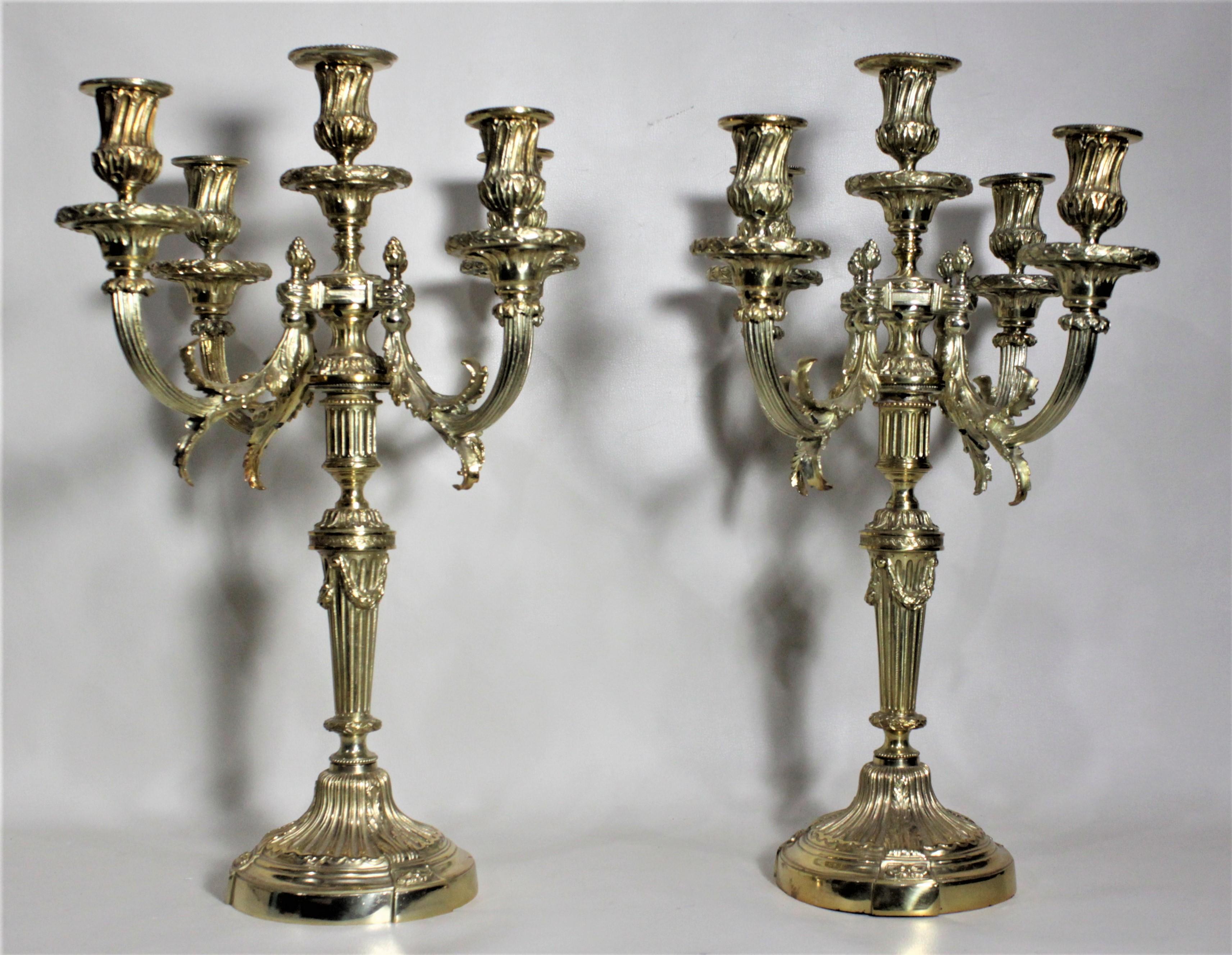 This pair of antique gilt candelabras are unmarked, but presumed to have been made in France between 1900 and 1920 in the Empire style. The candelabras are very ornately cast with scrolling leaves accenting each cup, and pineapple finials which