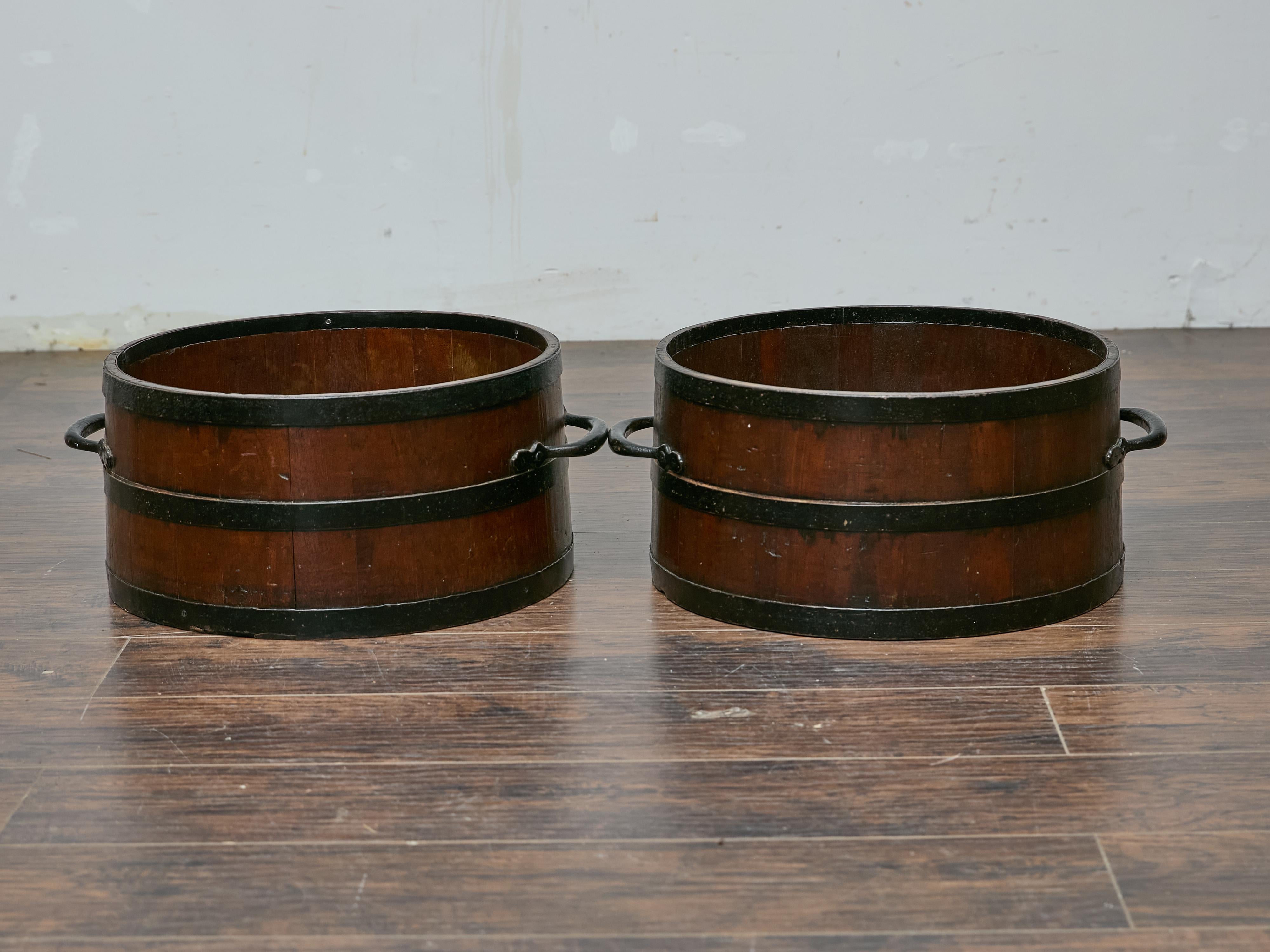 Cette paire de mesures de boisseau anglais antique apporte un charme rustique et une authenticité historique à n'importe quel espace. Fabriquées en bois avec des bandes de fer peintes en noir, ces mesures à grain du XIXe siècle au début du XXe