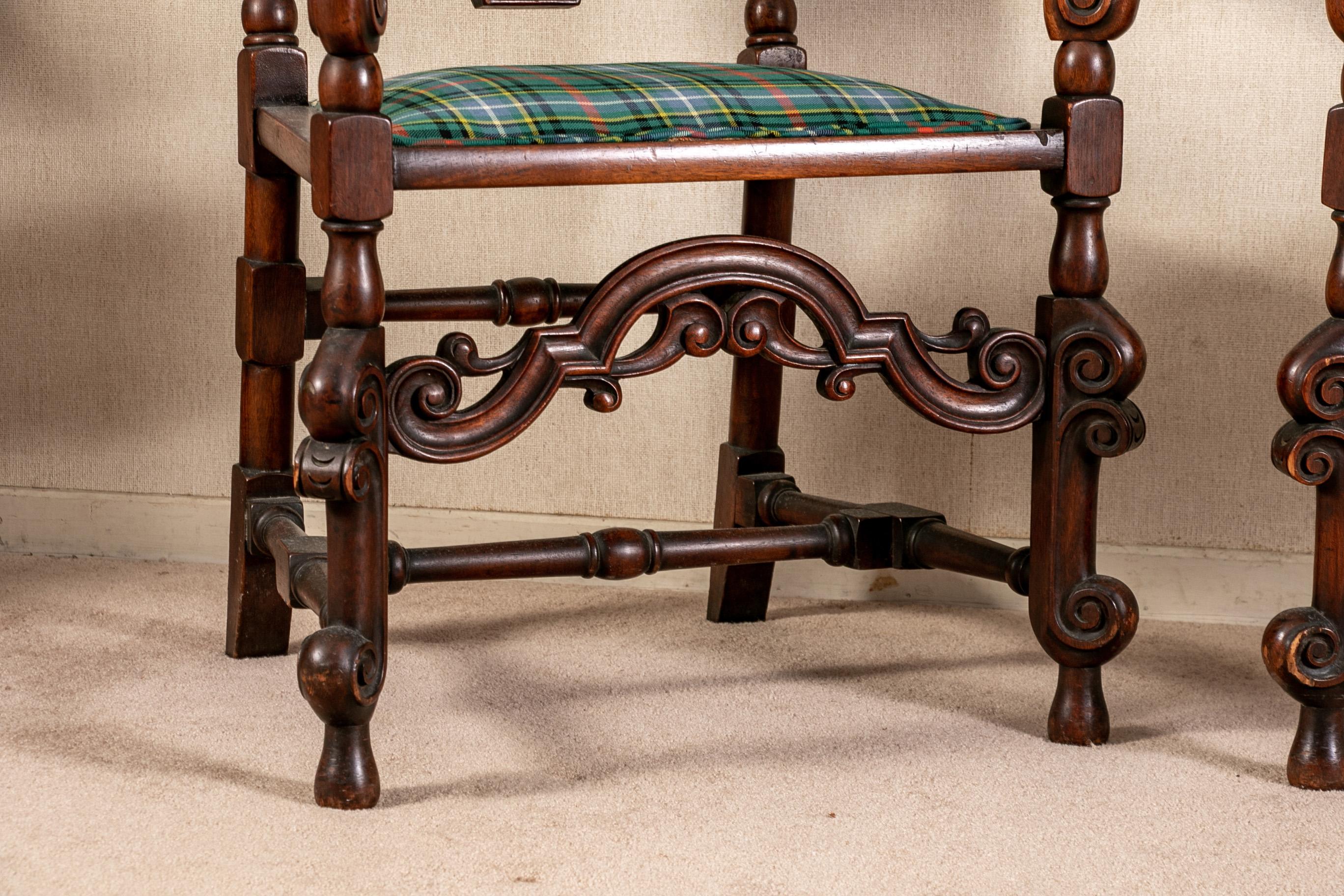Pair of antique English carved hall chairs in a tartan plaid, with openwork scrolled crest rails and front frames. Scrolled arms, turned legs and H stretchers, and a stretcher at the back. Blue plaid upholstery. Retailed by B. Altman & Co., New York