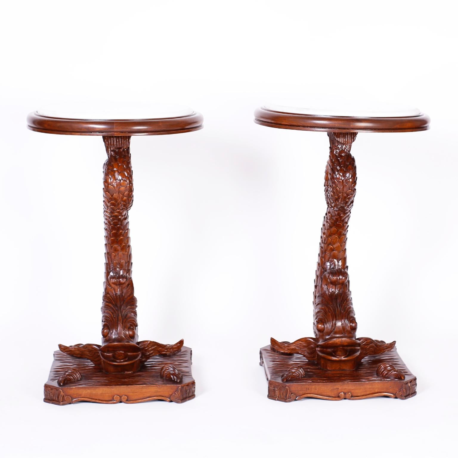 Impressive pair of antique British Colonial stands with white marble tops, crafted in mahogany and expertly carved depicting the mythological dolphins as described by ancient sailors. The bases depict water and sea shells over a classic scrolled