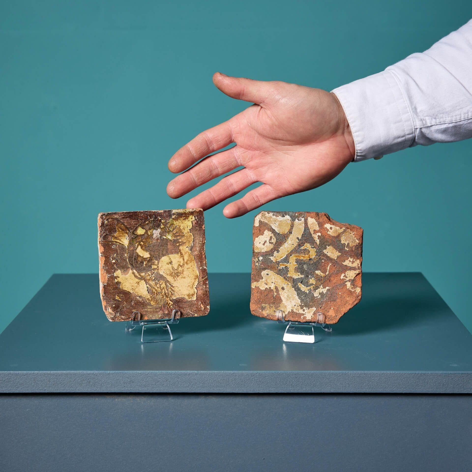 A pair of antique English encaustic medieval tiles, sourced from a private collection, Oxfordshire, dating to the 14-15th century.

The set comprises of two 10cm tiles displaying historical emblems in various mute colours, now hardly visible due to