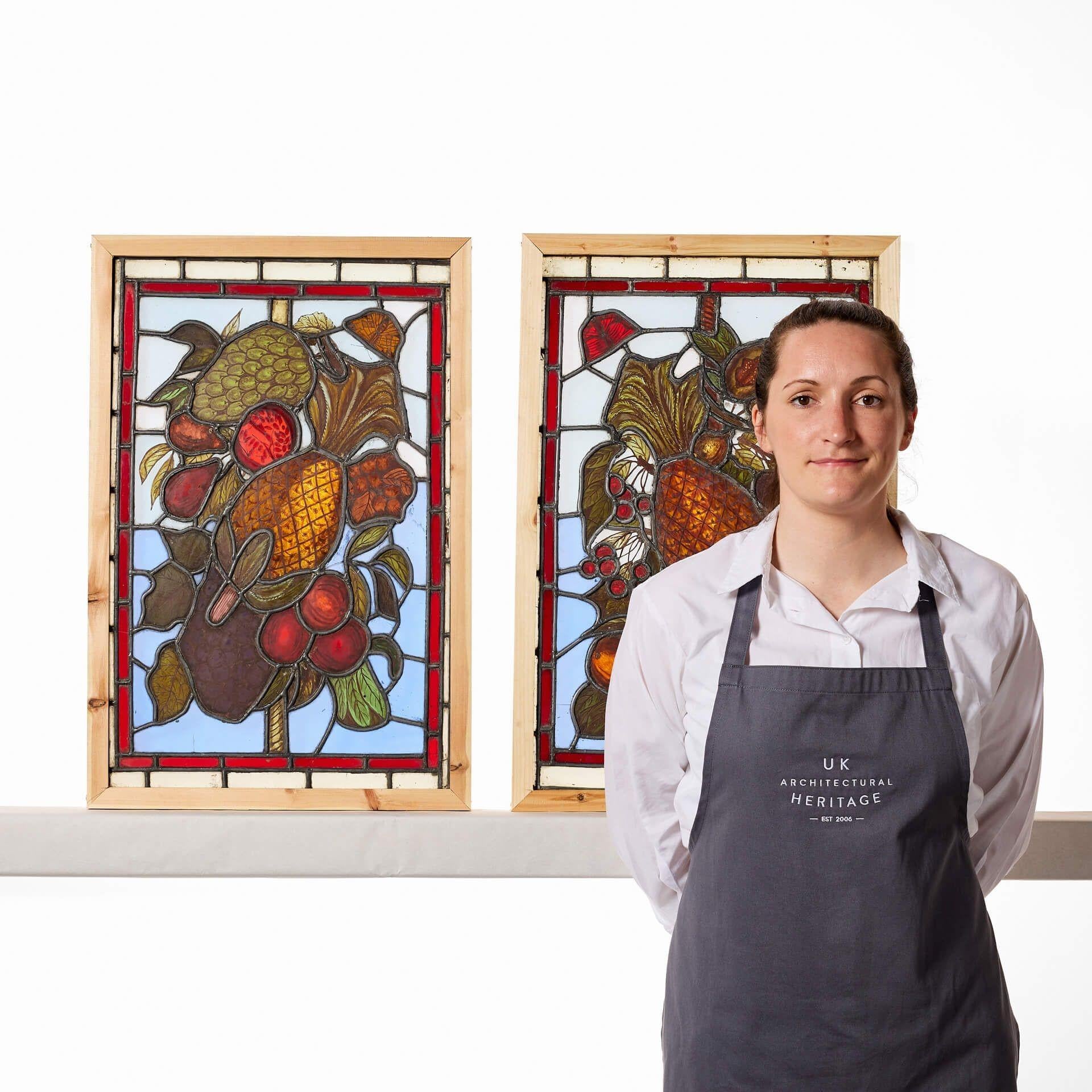 A beautiful pair of late 19th century antique English stained glass windows depicting an abundance of colourful fruits including pineapples, pomegranates, grapes and cherries alongside butterflies.

With slight variances in the design, these