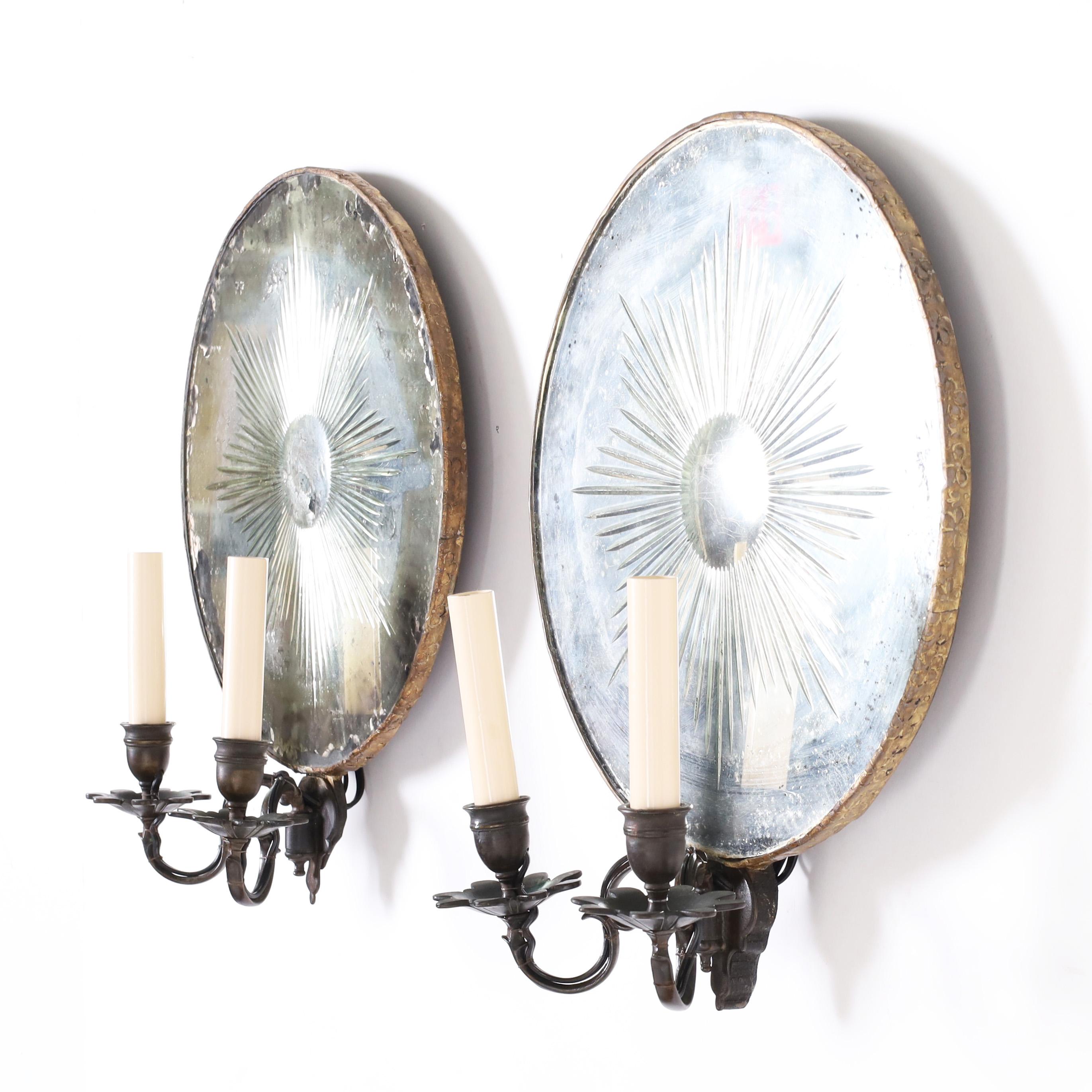 Lofty pair of 19th Century two light wall sconces, later electrified, featuring distressed mirrored backs with cut sun ray designs in a brass frame and graceful bronze floral arms and cups.