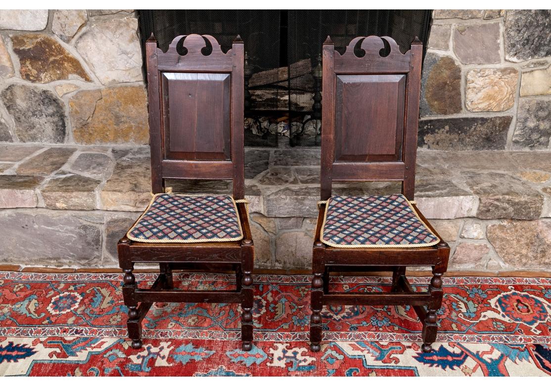 A fine pair of dark stained oak side chairs with carved crests, well turned legs, peg construction and panel backs. Traditional English form with good weight and construction. Custom tie on seat cushions with Diamond pattern fabric and rope trim and